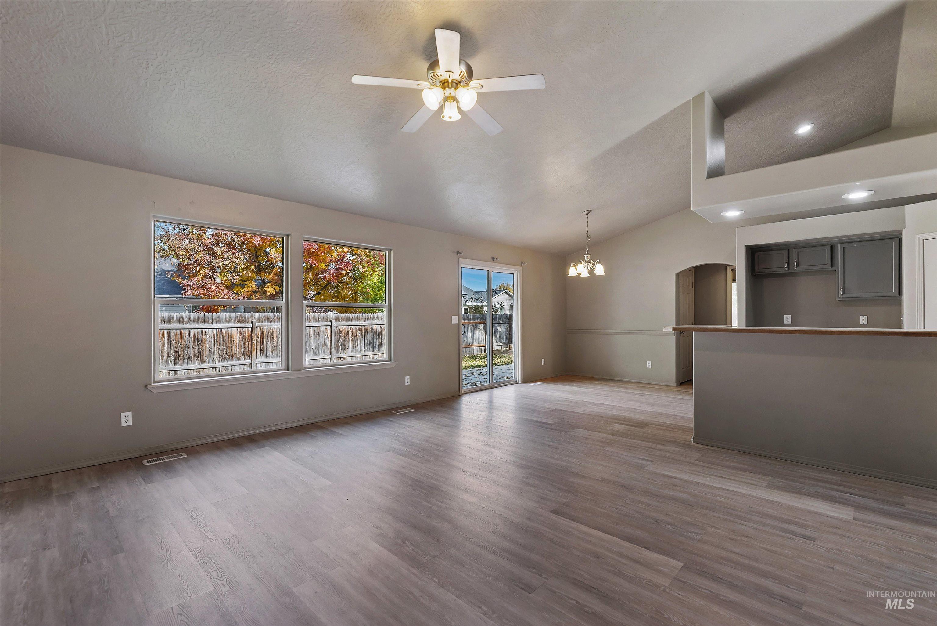 Unfurnished living room featuring wood finished floors, a ceiling fan, vaulted ceiling, recessed lighting, and arched walkways