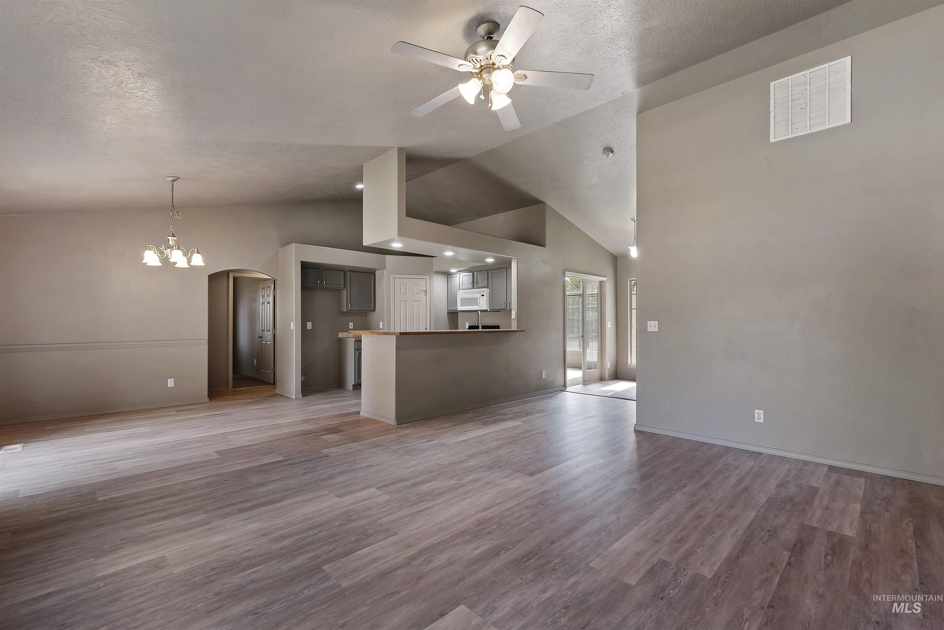 Unfurnished living room featuring arched walkways, wood finished floors, ceiling fan, high vaulted ceiling, and a chandelier