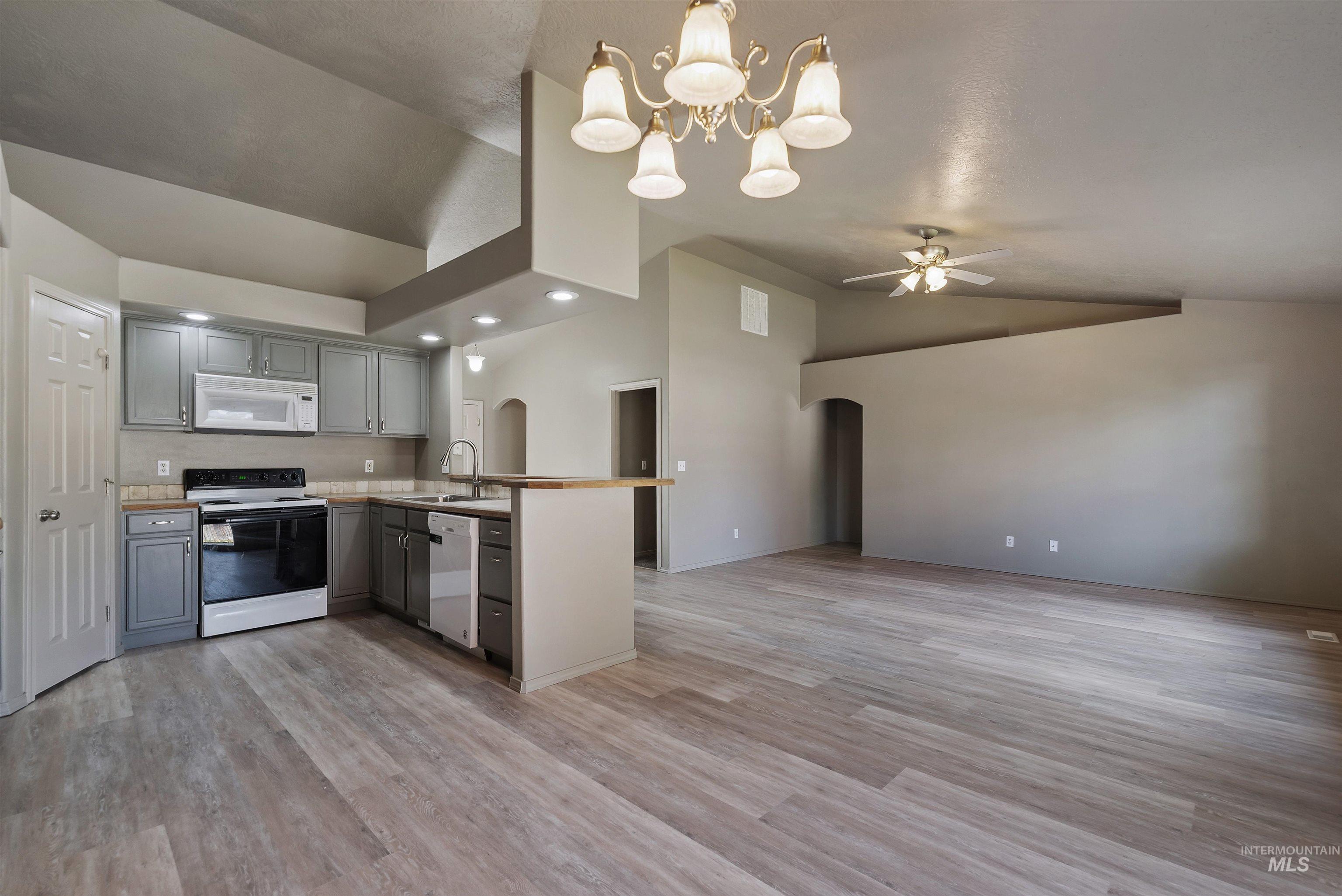 Kitchen featuring a peninsula, lofted ceiling, light countertops, a chandelier, and arched walkways