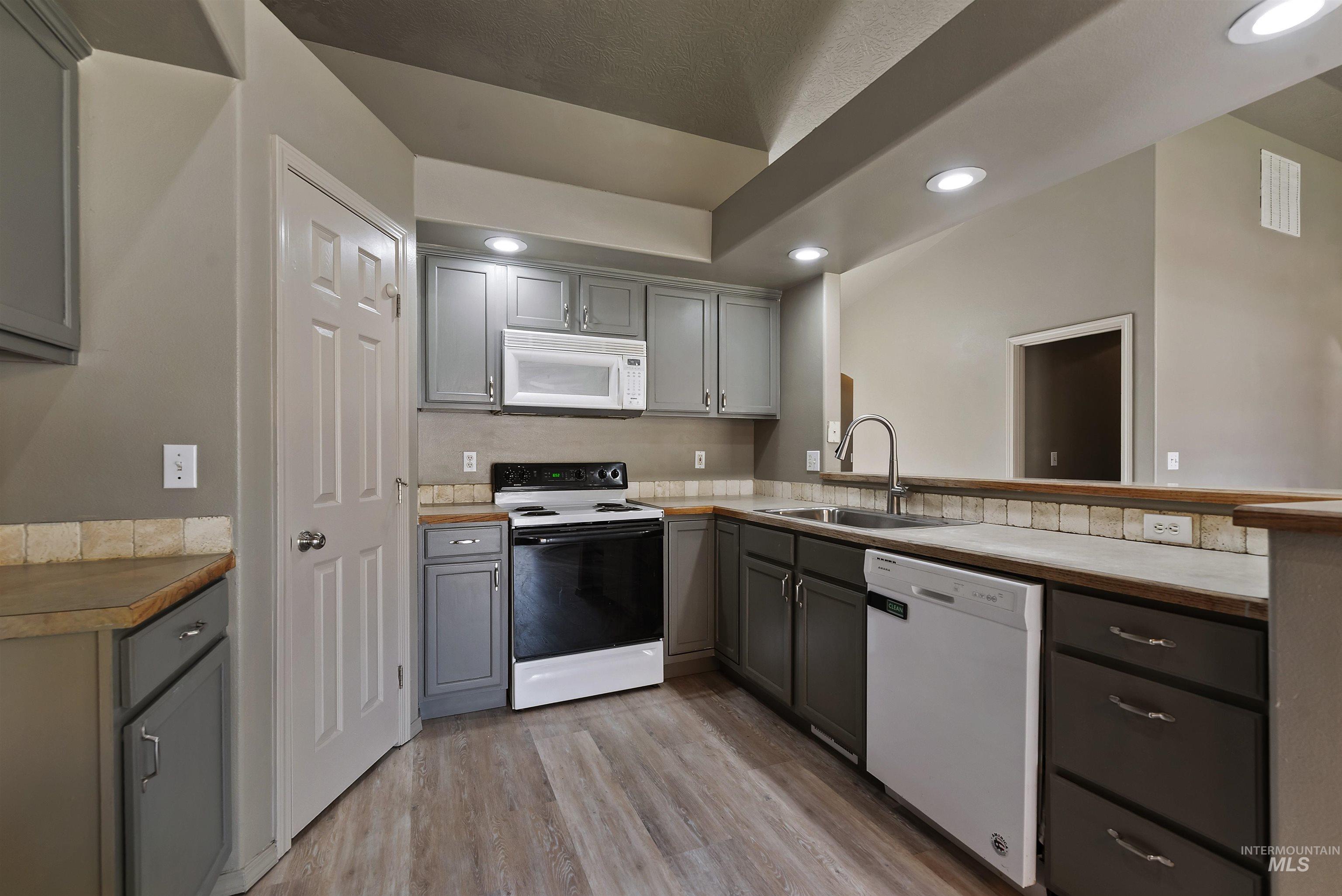 Kitchen with gray cabinets, white appliances, light wood-type flooring, recessed lighting, and tasteful backsplash