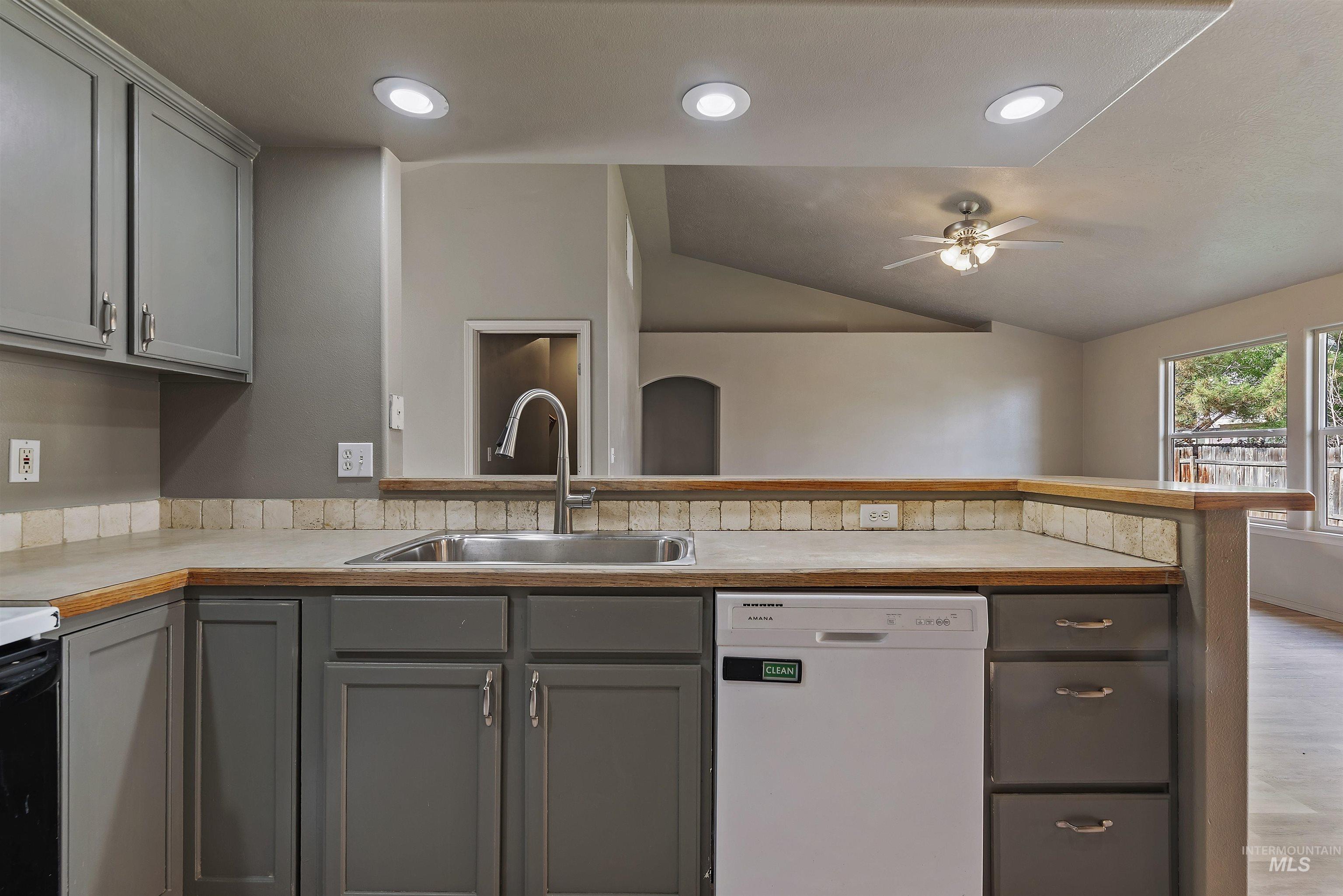 Kitchen featuring gray cabinetry, white dishwasher, light countertops, lofted ceiling, and recessed lighting