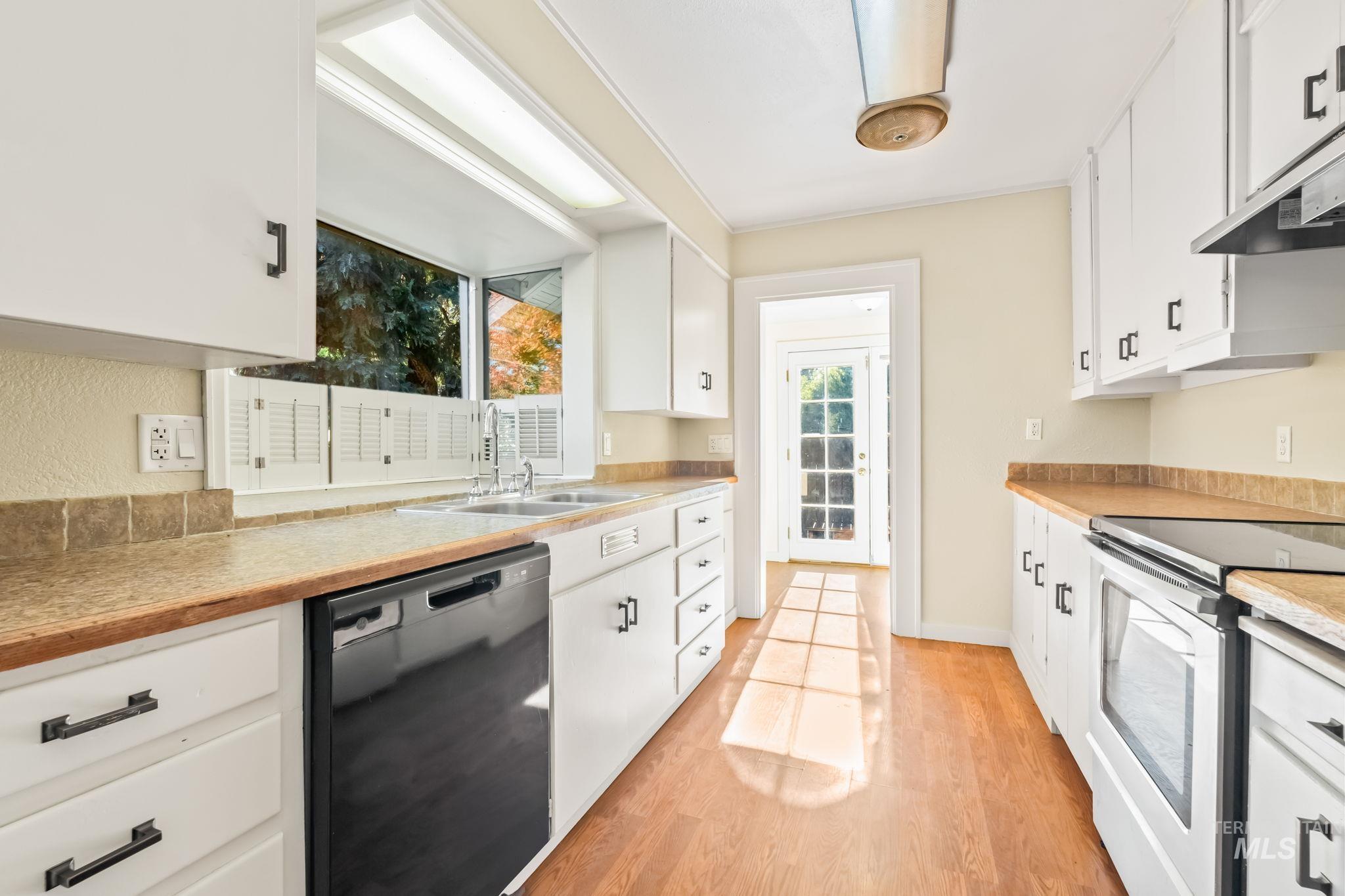 Kitchen with white cabinetry, black dishwasher, light countertops, and light wood-style flooring