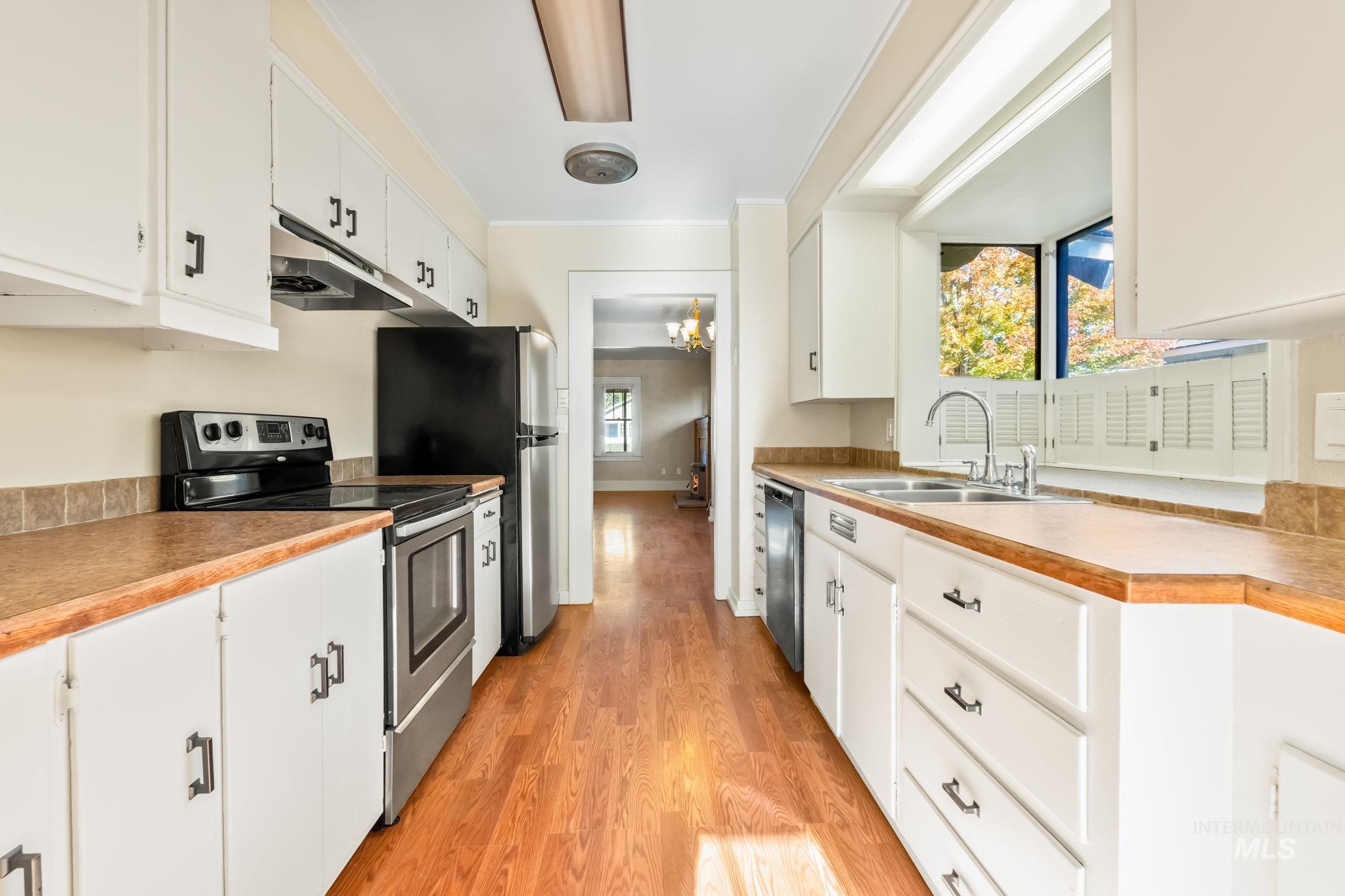 Kitchen featuring stainless steel appliances, white cabinets, light wood-style flooring, ornamental molding, and under cabinet range hood