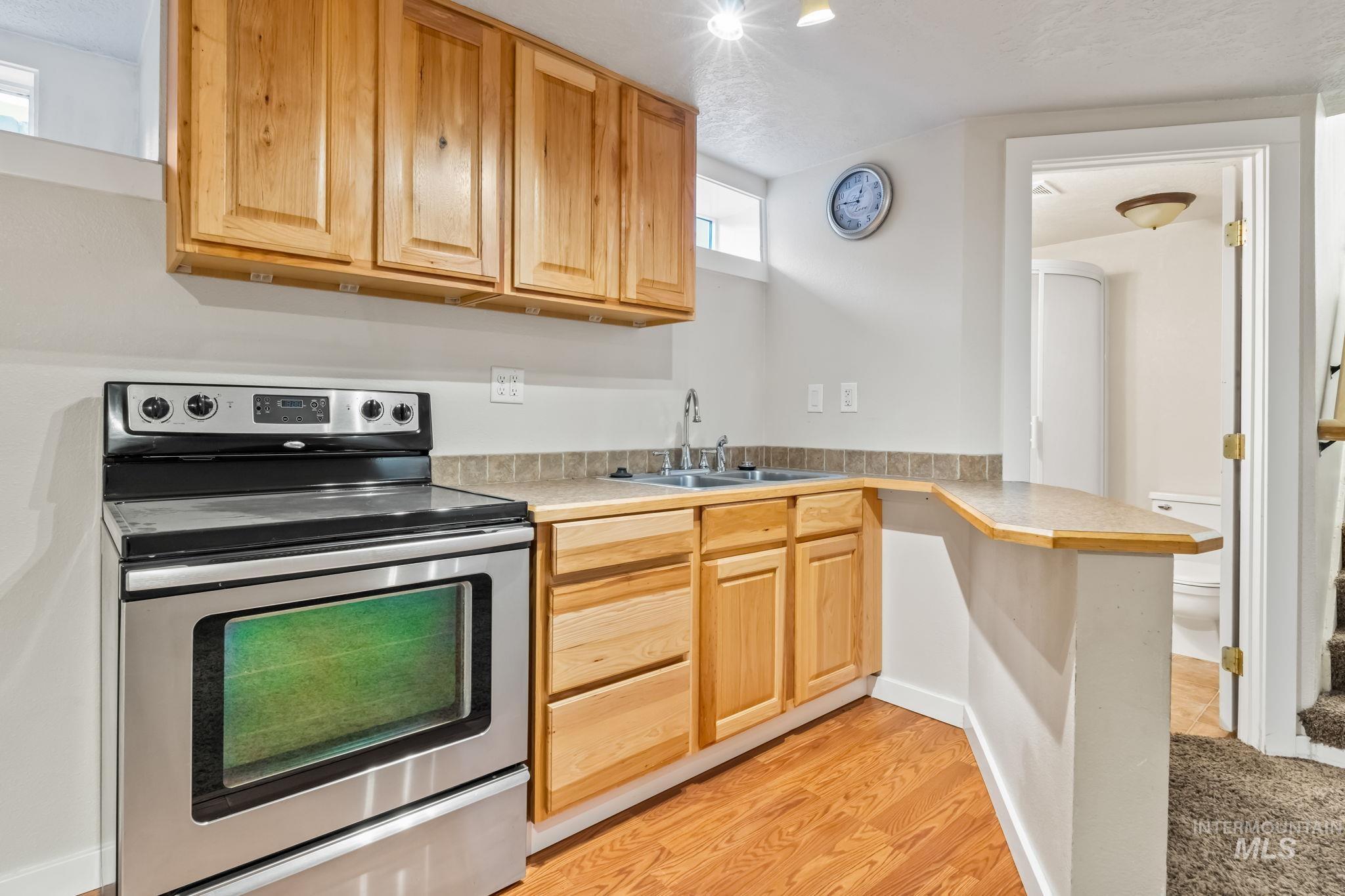Kitchen featuring stainless steel electric range oven, light countertops, a peninsula, light wood-style flooring, and light brown cabinetry