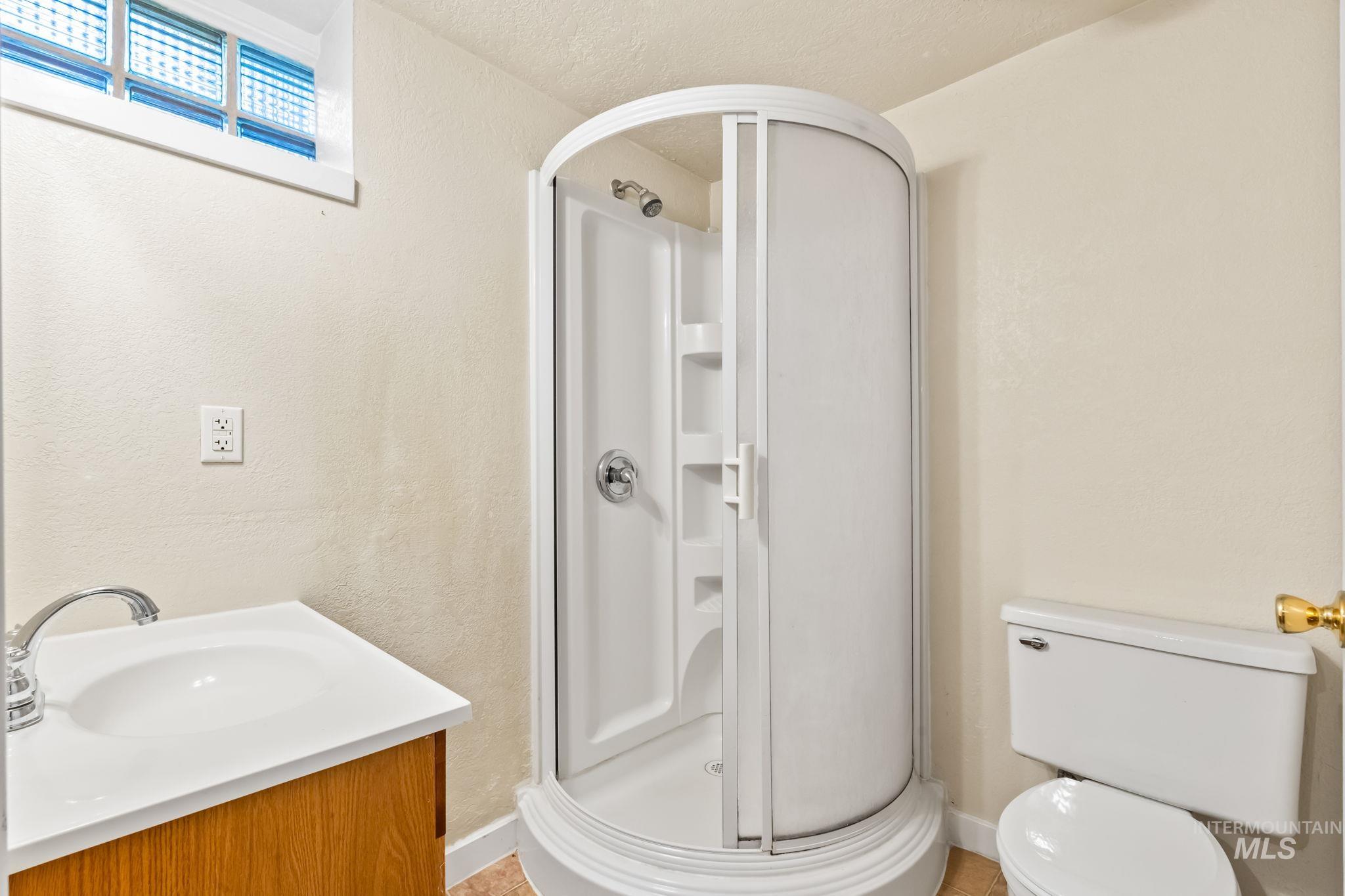 Full bathroom with vanity, a textured wall, a stall shower, light tile patterned flooring, and a textured ceiling