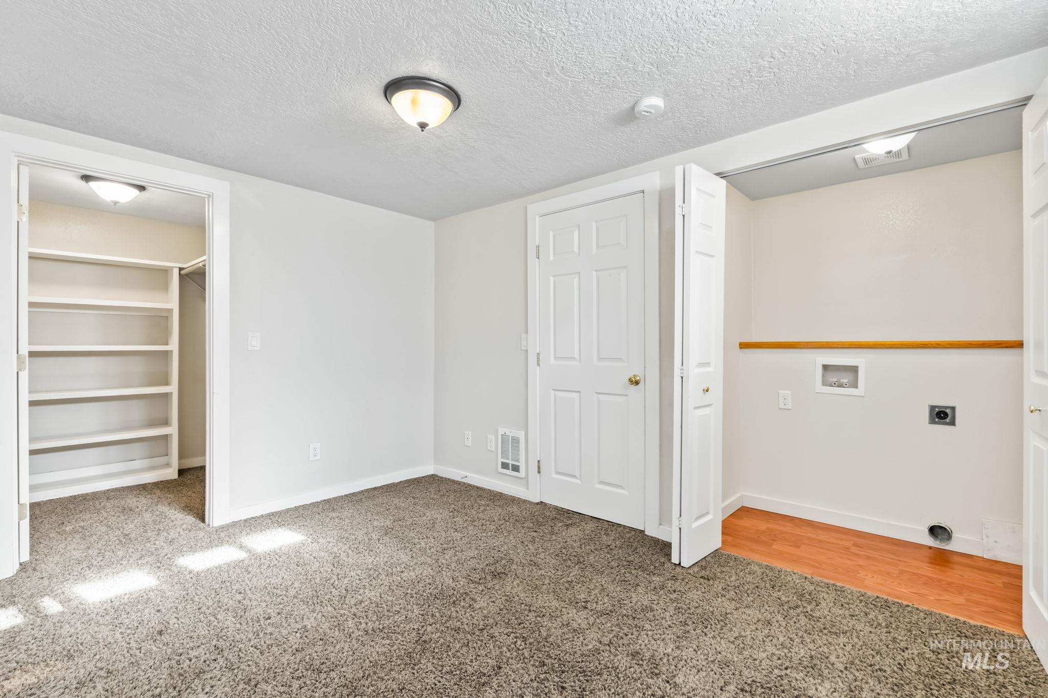 Unfurnished bedroom featuring light colored carpet, a textured ceiling, a walk in closet, and light wood-style flooring