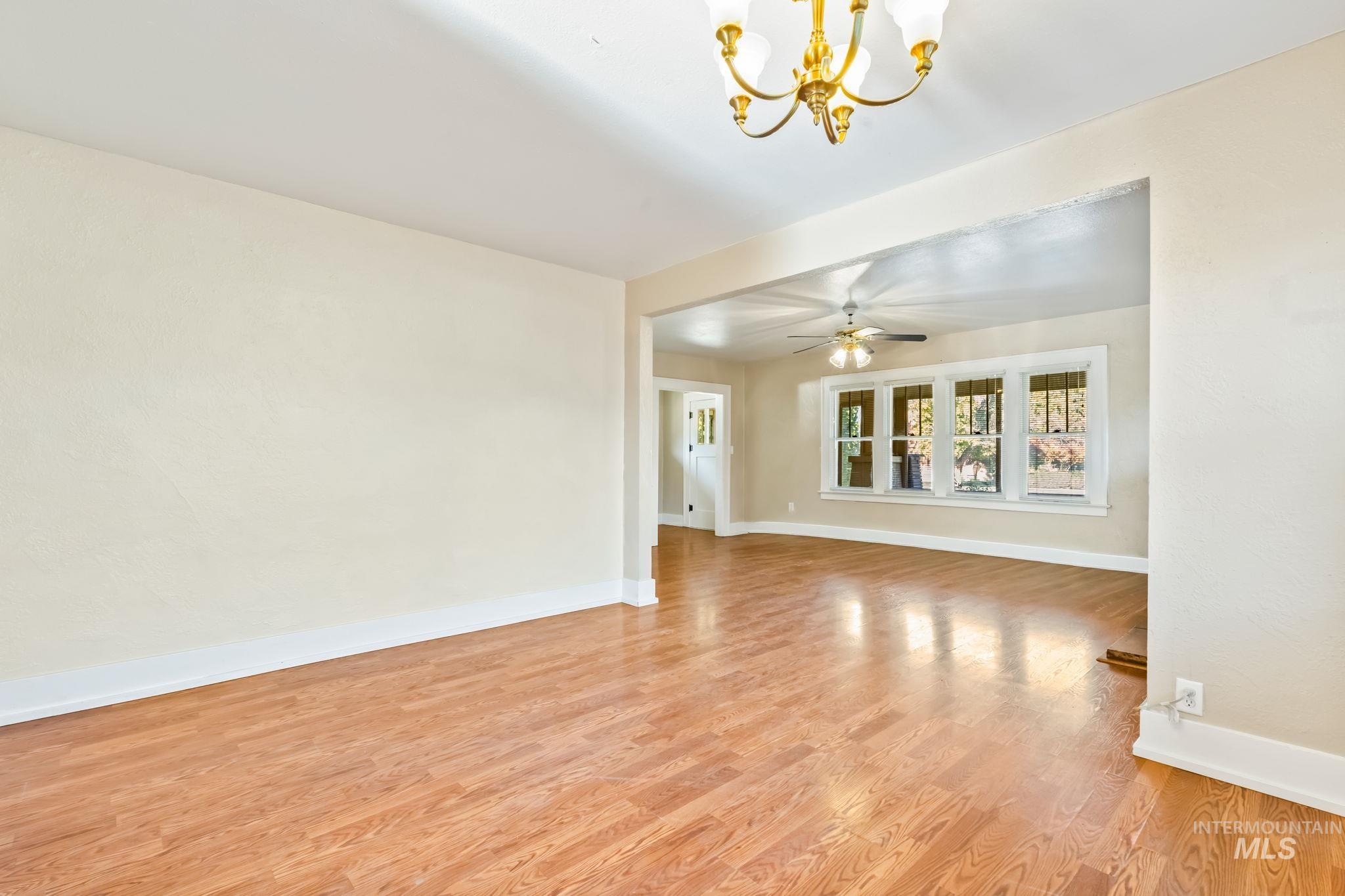Empty room with light wood-type flooring, a chandelier, and ceiling fan