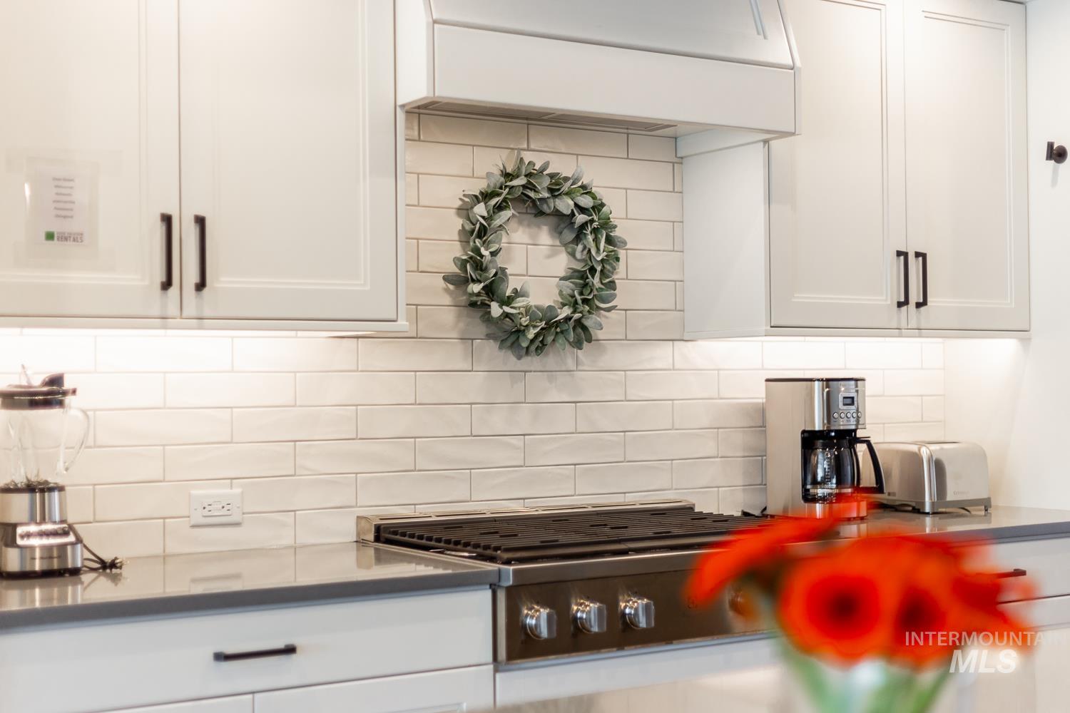 Kitchen featuring tasteful backsplash, white cabinets, premium range hood, and stainless steel gas stovetop
