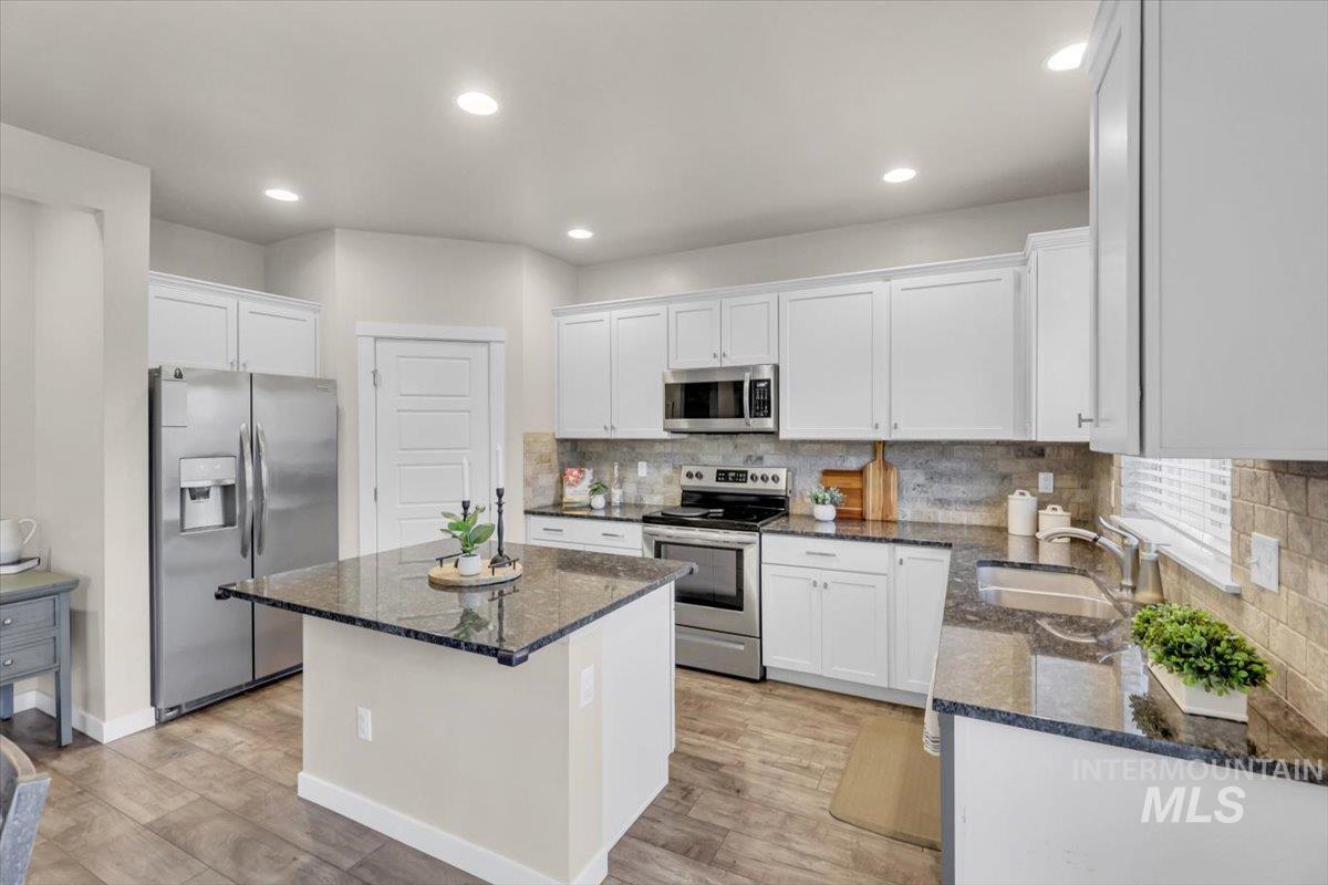 Kitchen with stainless steel appliances, dark stone countertops, white cabinets, a center island, and recessed lighting