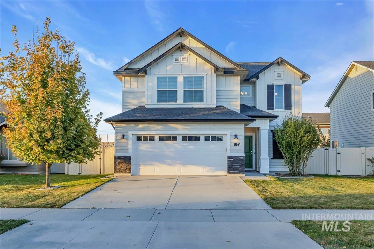 Craftsman-style home with board and batten siding, a garage, driveway, a gate, and stone siding
