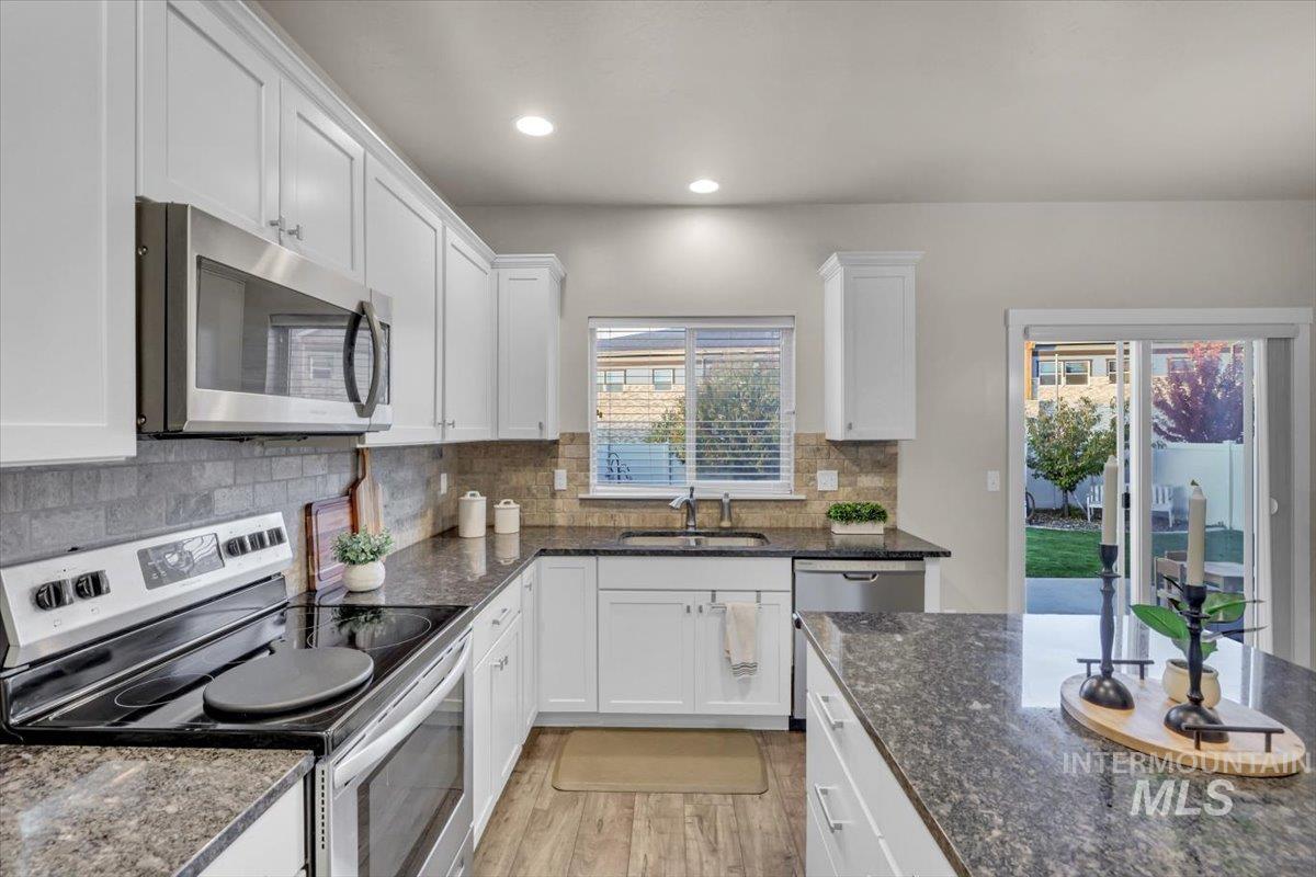 Kitchen featuring appliances with stainless steel finishes, dark stone countertops, white cabinets, backsplash, and recessed lighting