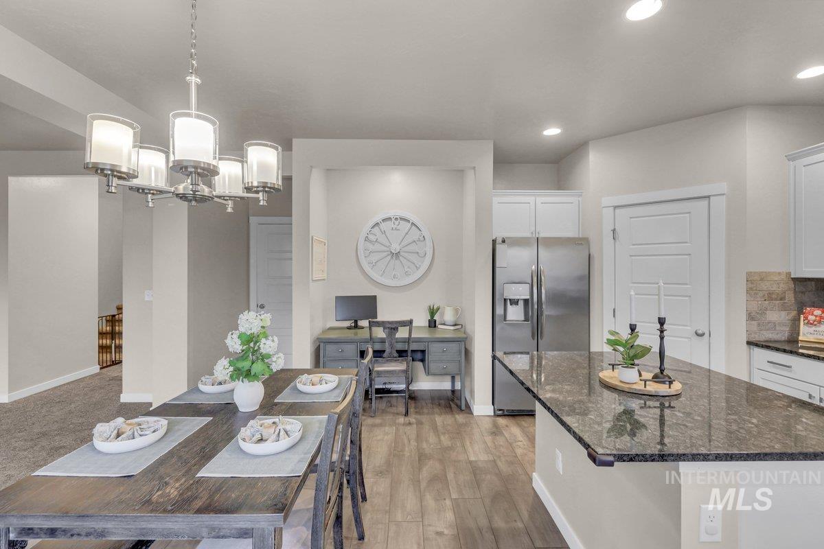 Kitchen with dark stone counters, stainless steel refrigerator with ice dispenser, white cabinetry, light wood-style floors, and decorative light fixtures