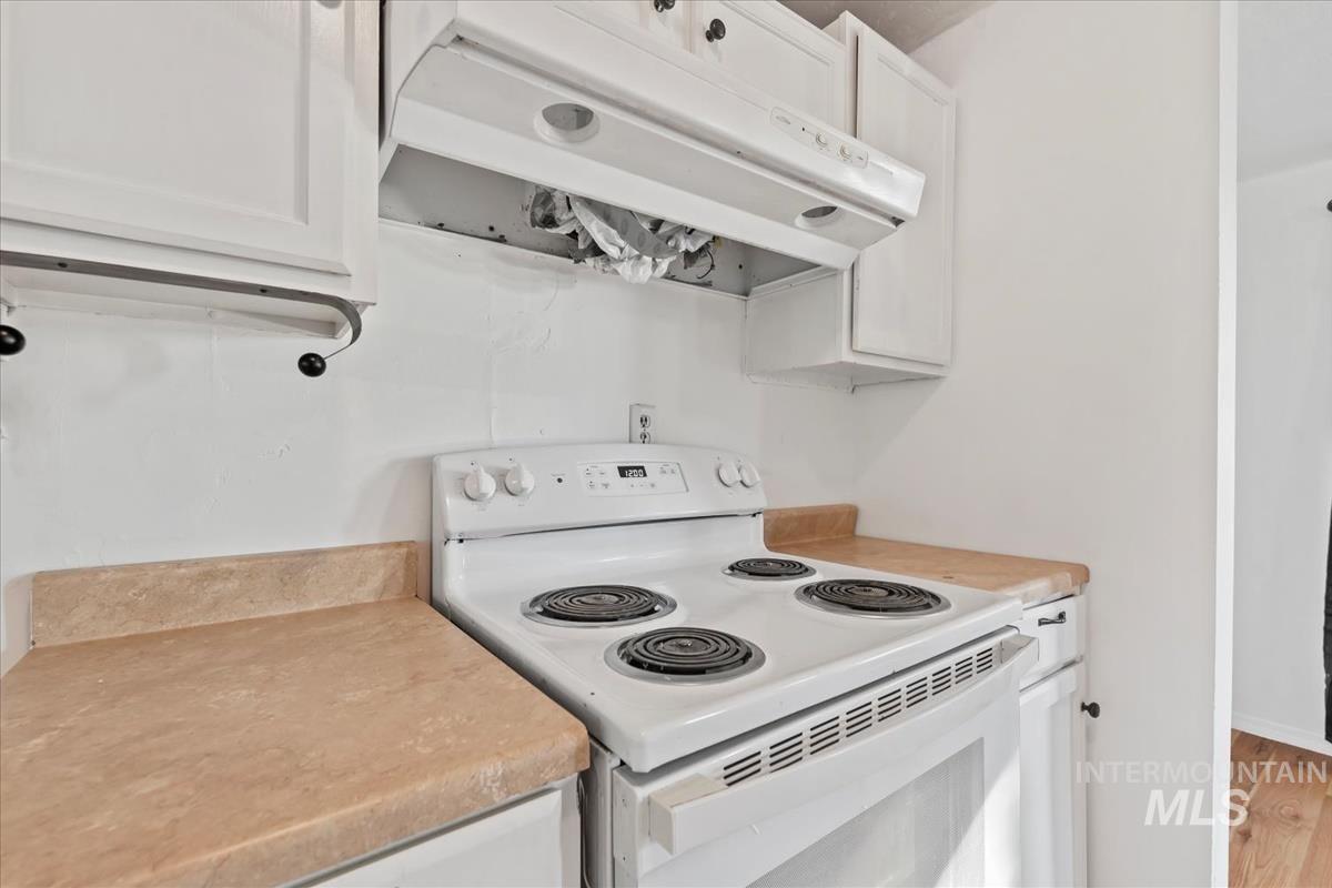 Kitchen with white electric stove, under cabinet range hood, white cabinetry, and light countertops