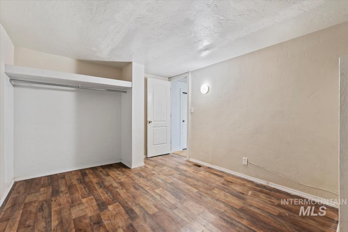 Unfurnished bedroom with a textured ceiling, wood finished floors, a closet, and a textured wall