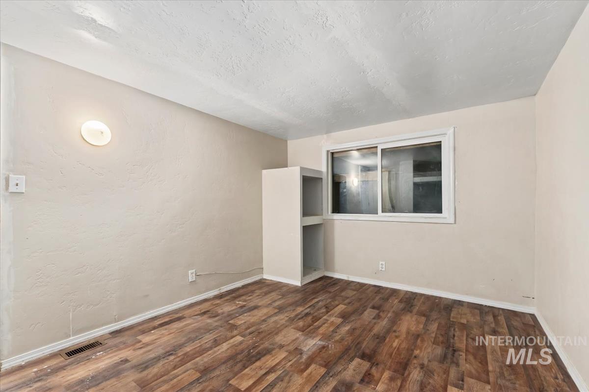 Spare room featuring a textured ceiling, dark wood-type flooring, and a textured wall