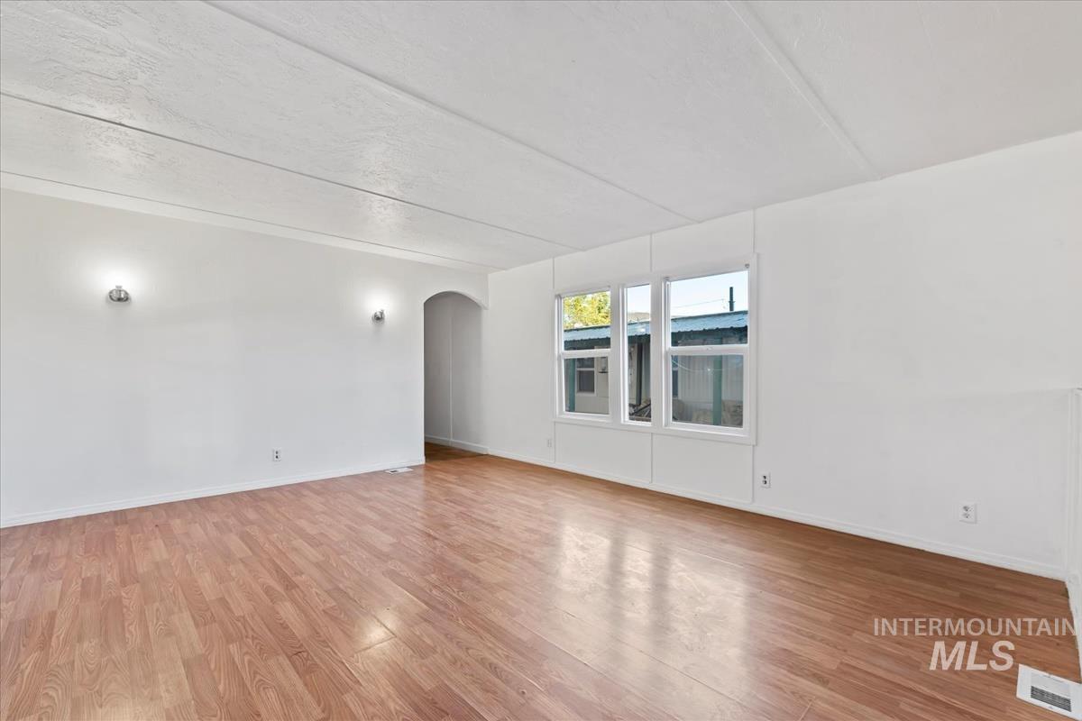 Empty room featuring arched walkways, light wood finished floors, and a textured ceiling