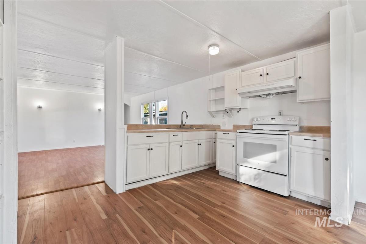 Kitchen featuring white cabinets, white range with electric stovetop, light wood-style flooring, under cabinet range hood, and open shelves