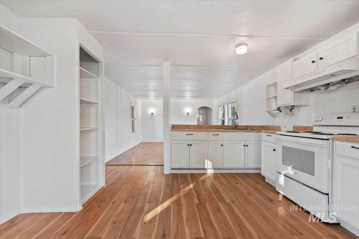 Kitchen featuring white electric range, open shelves, white cabinets, under cabinet range hood, and a peninsula