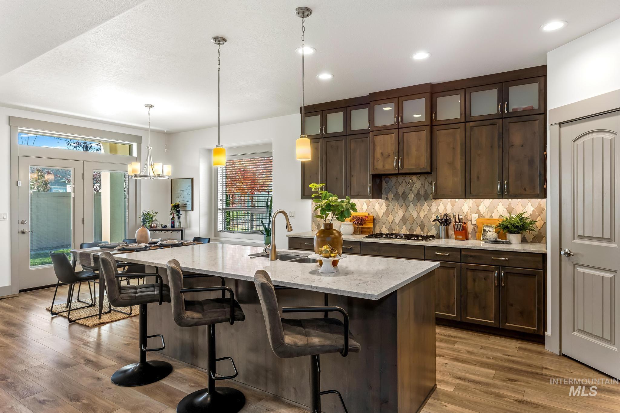 Kitchen featuring dark brown cabinetry, decorative backsplash, a kitchen bar, hanging light fixtures, and light stone countertops