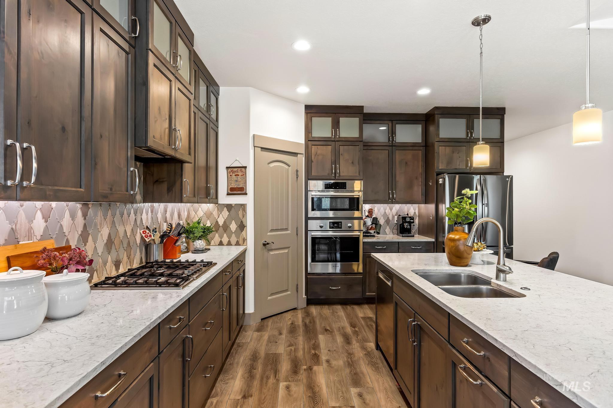 Kitchen featuring dark brown cabinets, pendant lighting, glass insert cabinets, stainless steel appliances, and recessed lighting