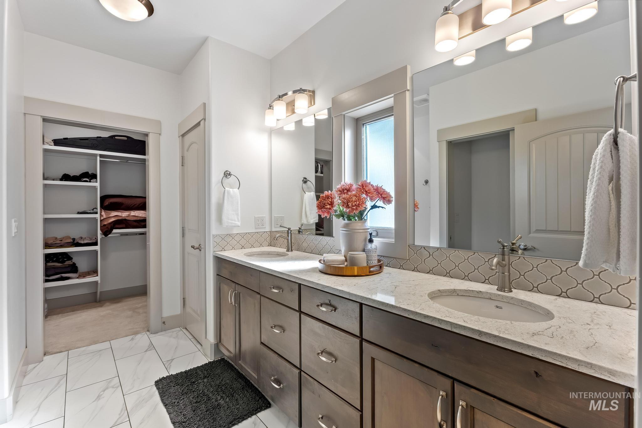 Bathroom with double vanity, tasteful backsplash, light marble finish flooring, and a walk in closet