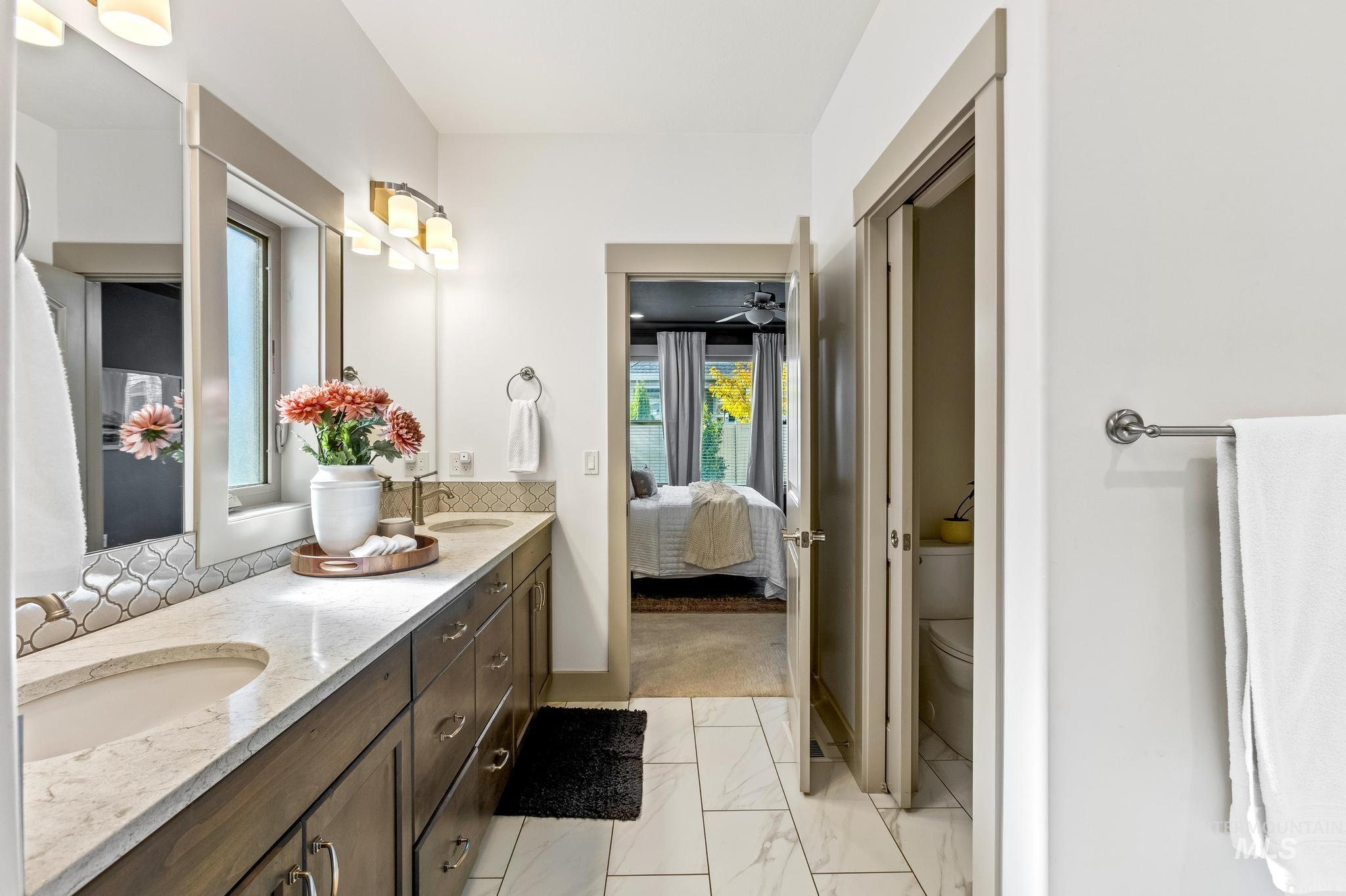 Ensuite bathroom with double vanity, light marble finish flooring, ceiling fan, and backsplash