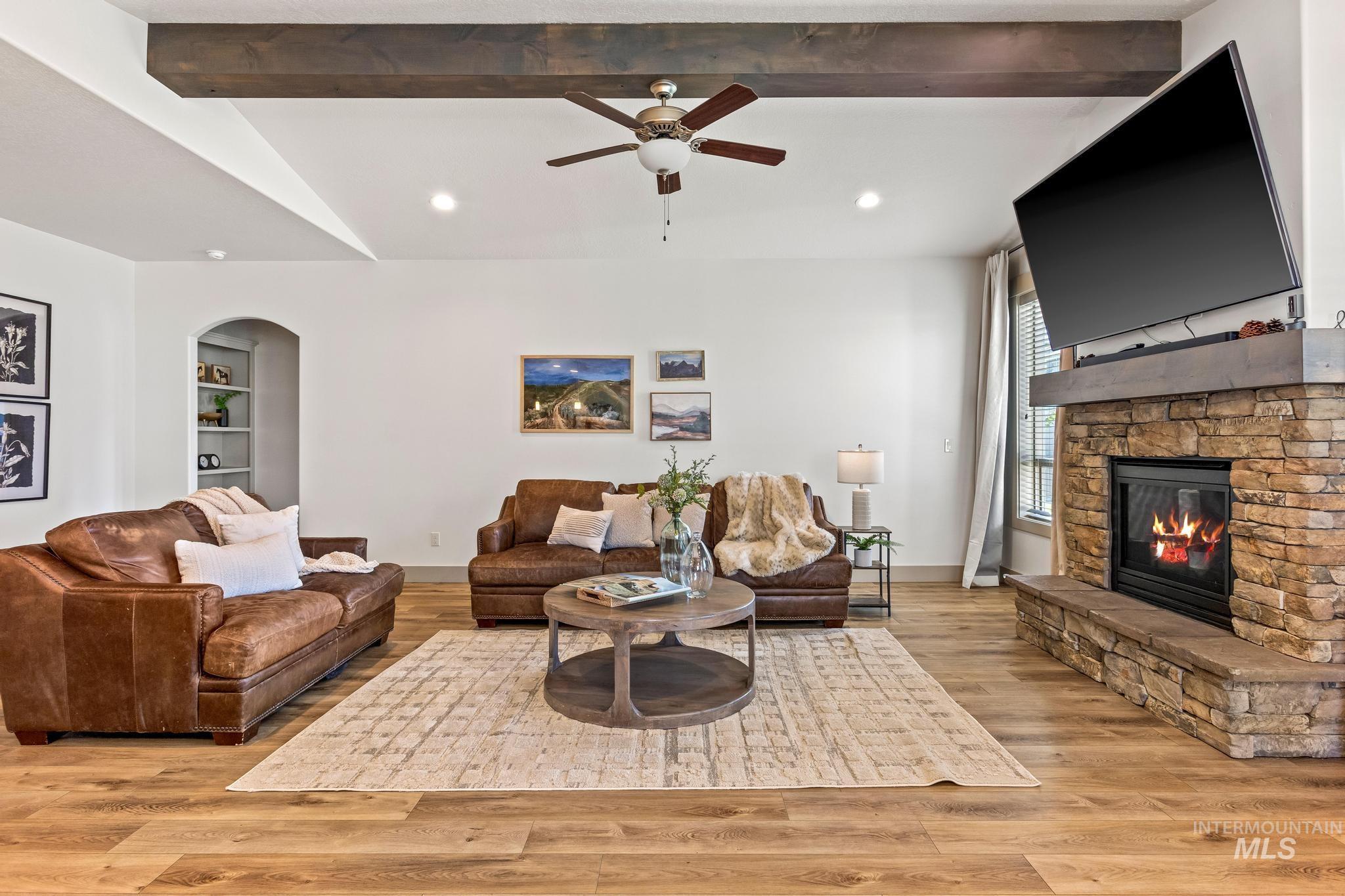 Living area featuring light wood-style flooring, ceiling fan, arched walkways, recessed lighting, and a stone fireplace