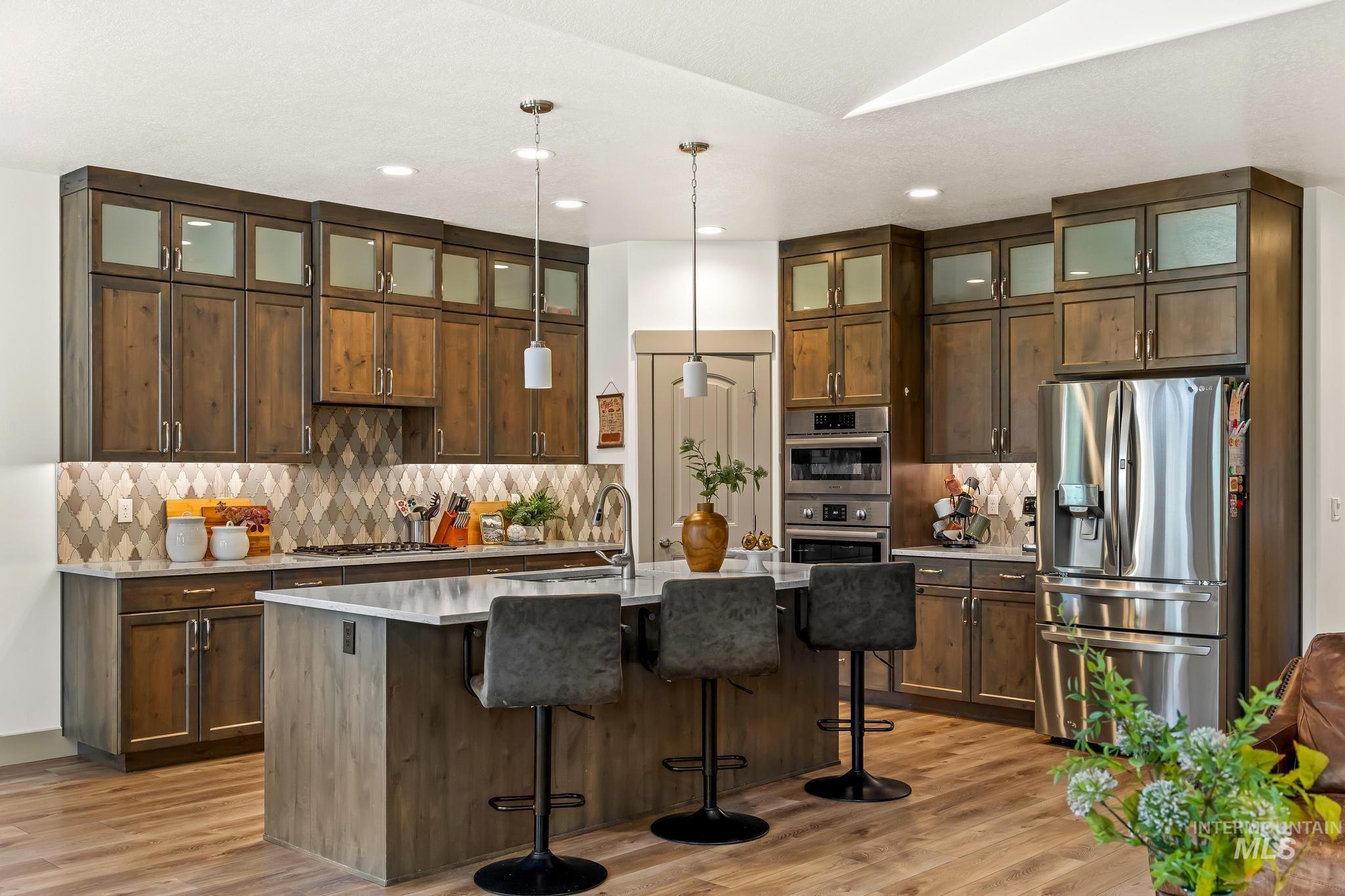 Kitchen featuring appliances with stainless steel finishes, decorative light fixtures, a center island with sink, tasteful backsplash, and a kitchen bar