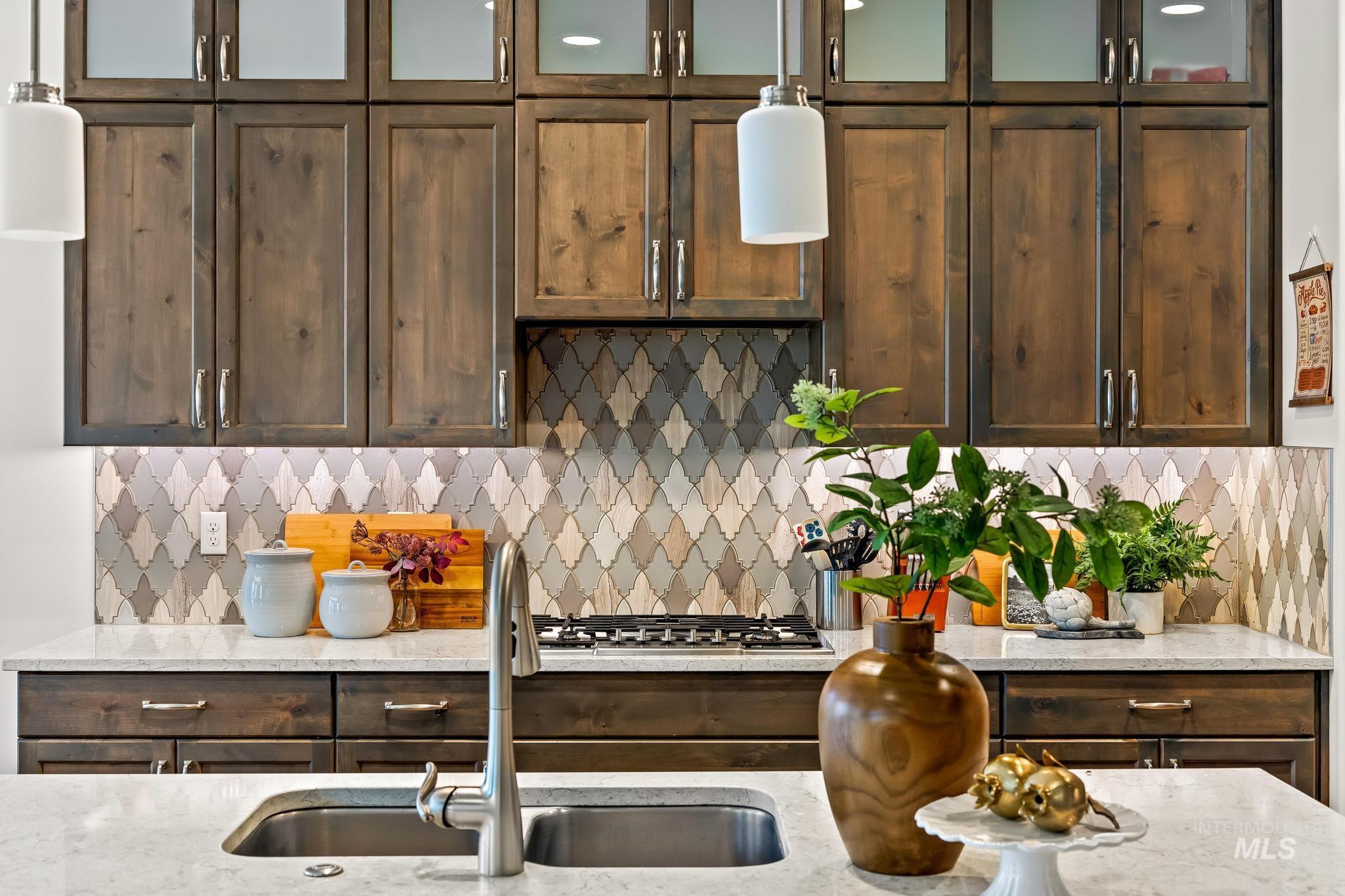 Kitchen with tasteful backsplash, light stone counters, dark brown cabinetry, hanging light fixtures, and glass insert cabinets