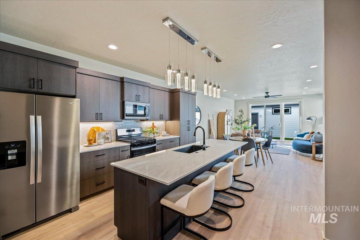 Kitchen with appliances with stainless steel finishes, a kitchen breakfast bar, pendant lighting, a textured ceiling, and a center island with sink