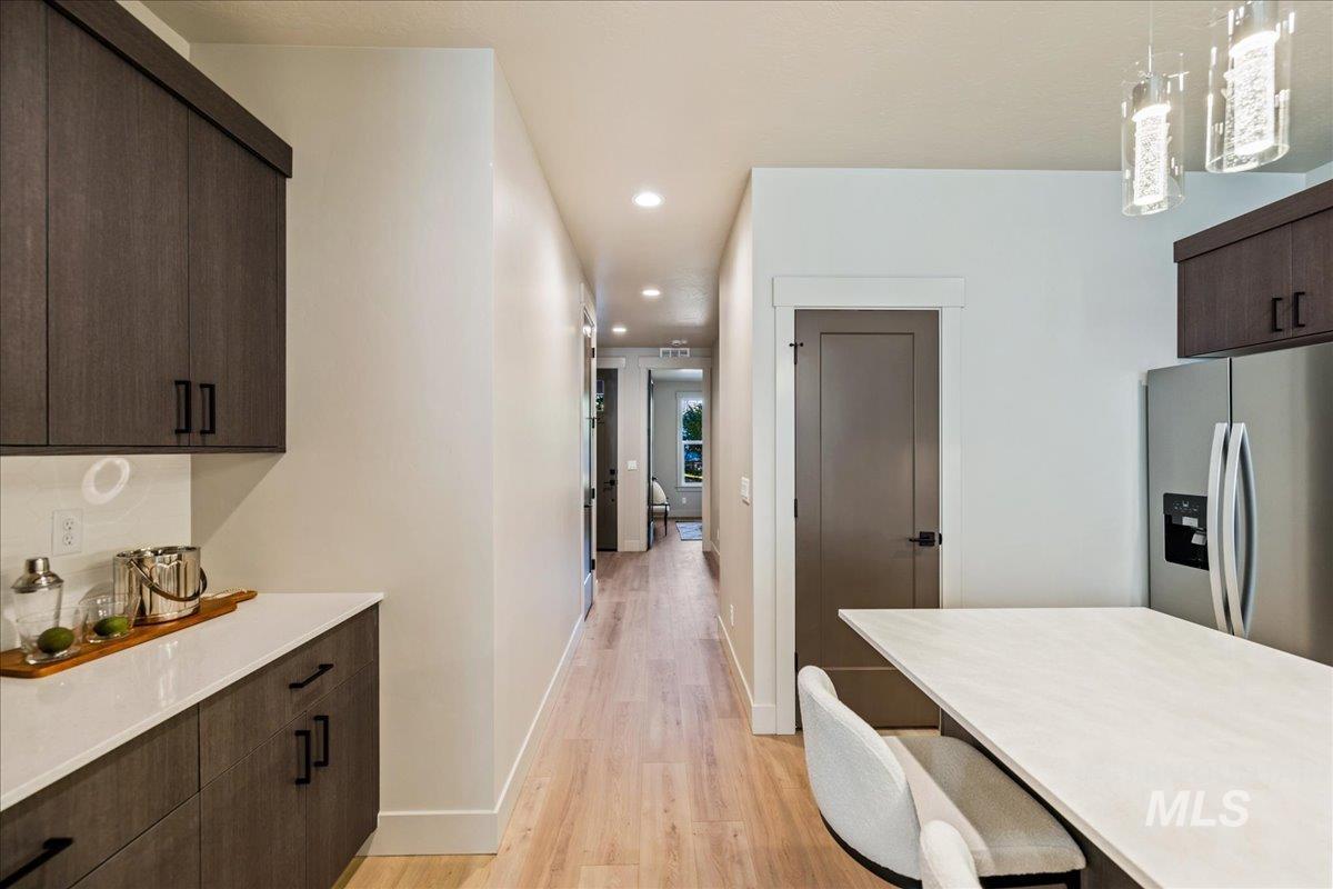 Kitchen with dark brown cabinetry, stainless steel fridge with ice dispenser, modern cabinets, recessed lighting, and light wood-type flooring