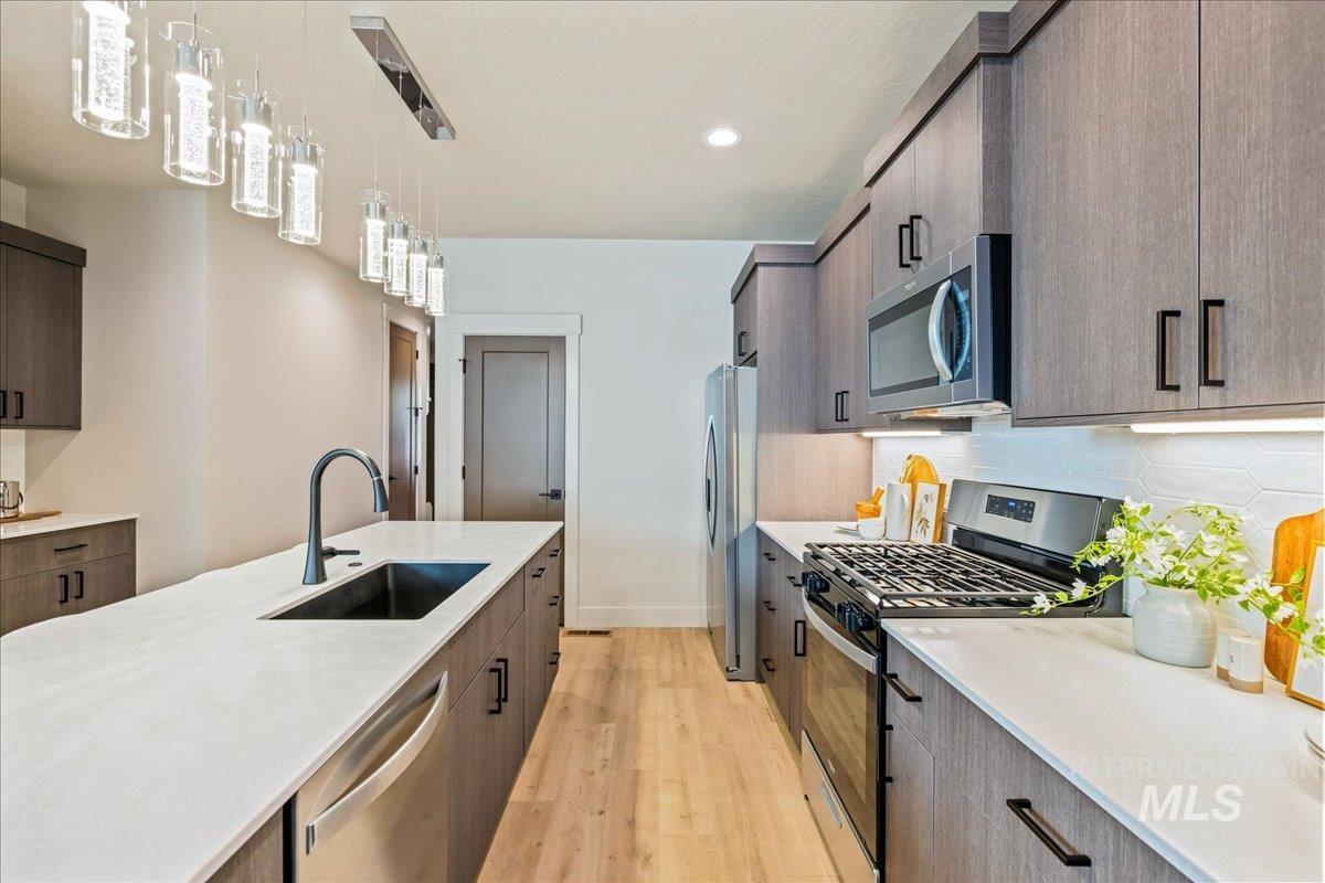 Kitchen featuring modern cabinets, stainless steel appliances, hanging light fixtures, light stone countertops, and light wood-type flooring
