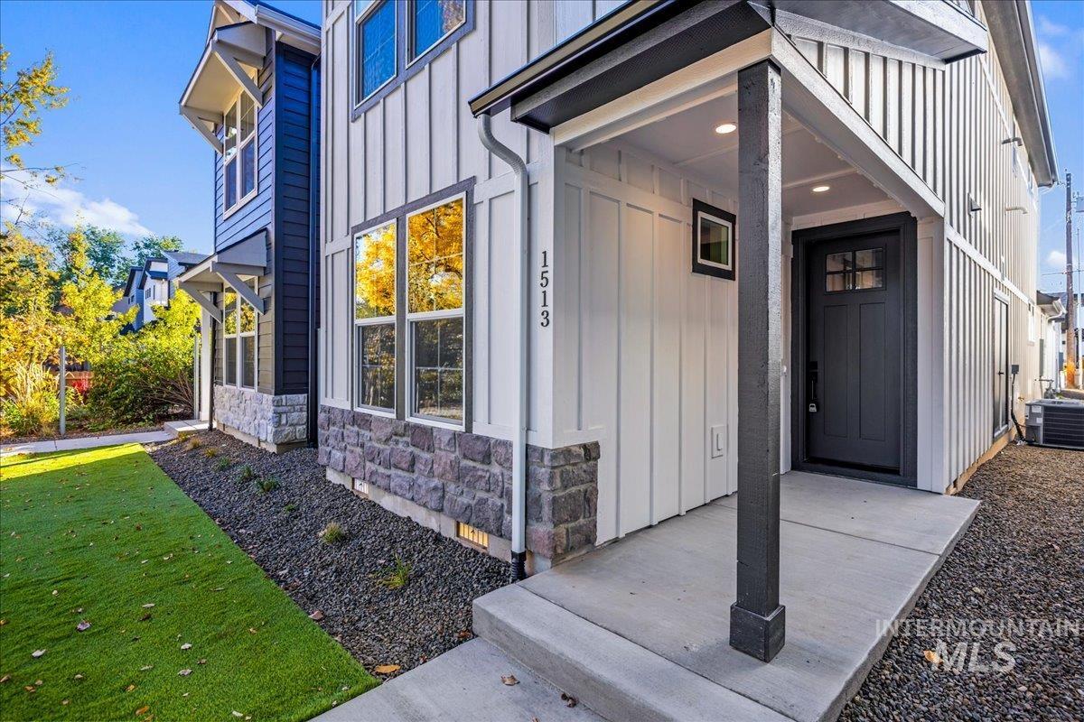 View of exterior entry with board and batten siding, stone siding, and a lawn
