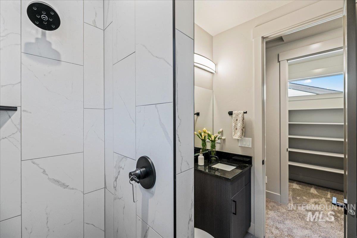 Full bath with vanity, tiled shower, and light colored carpet