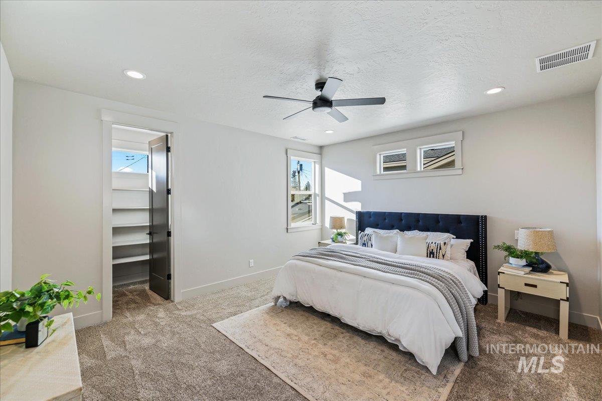 Bedroom with carpet, multiple windows, a spacious closet, a textured ceiling, and ceiling fan
