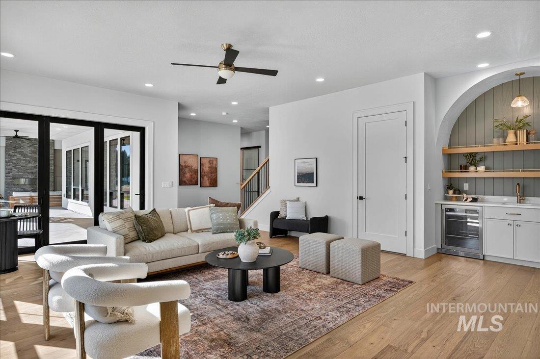 Living area with ceiling fan, wine cooler, bar with sink, light wood finished floors, and recessed lighting