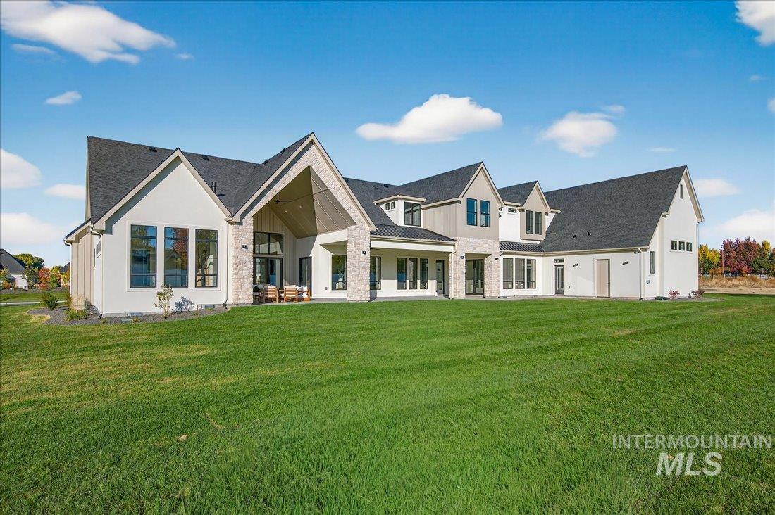 Back of property featuring stone siding, a lawn, a patio area, and roof with shingles