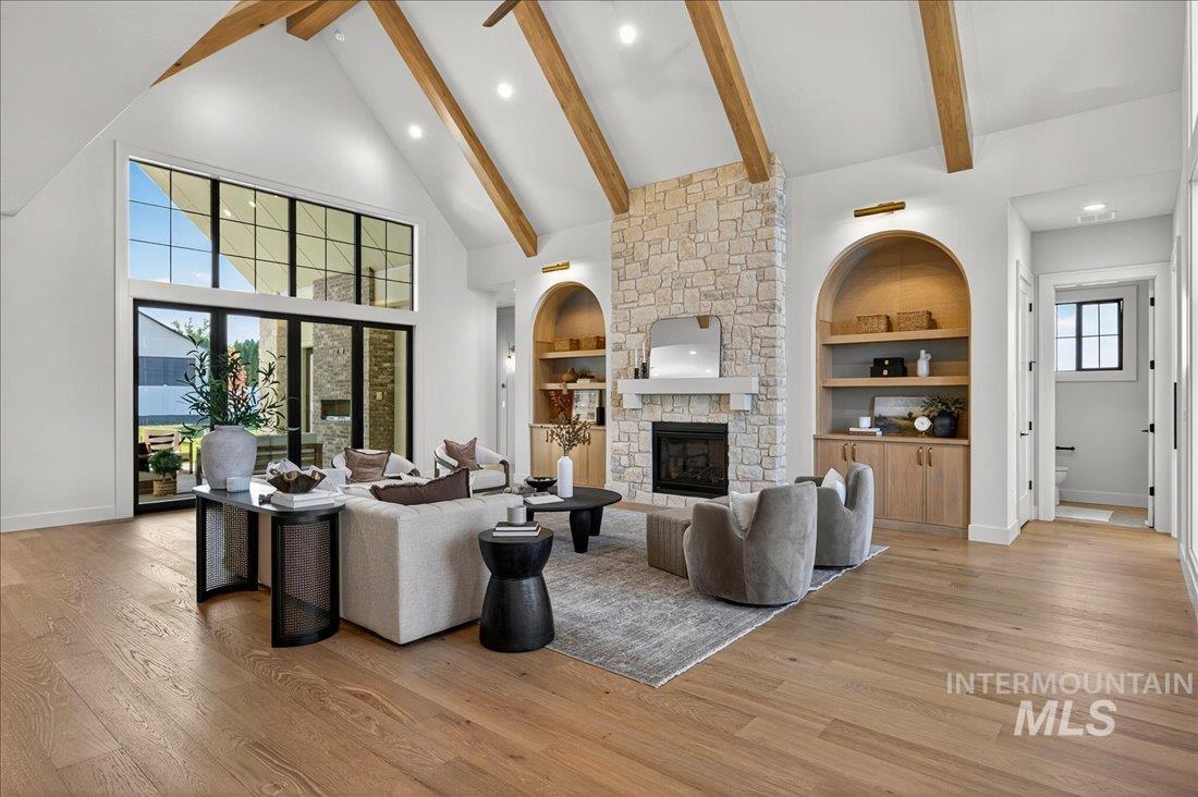 Living room with high vaulted ceiling, a fireplace, built in features, light wood-style floors, and beam ceiling