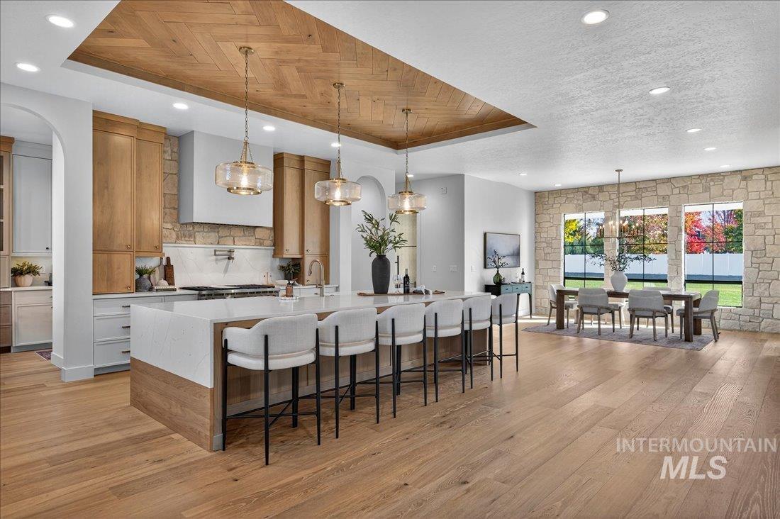 Kitchen with pendant lighting, light stone countertops, light wood finished floors, a raised ceiling, and recessed lighting