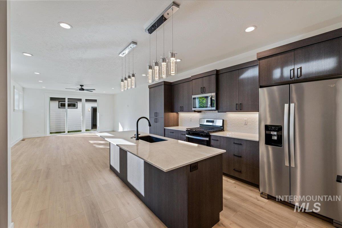 Kitchen featuring stainless steel appliances, pendant lighting, a center island with sink, open floor plan, and light wood-style floors