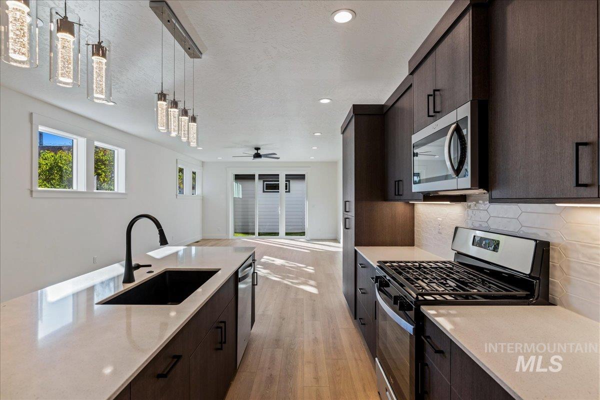 Kitchen featuring stainless steel appliances, dark brown cabinetry, modern cabinets, decorative light fixtures, and light wood finished floors