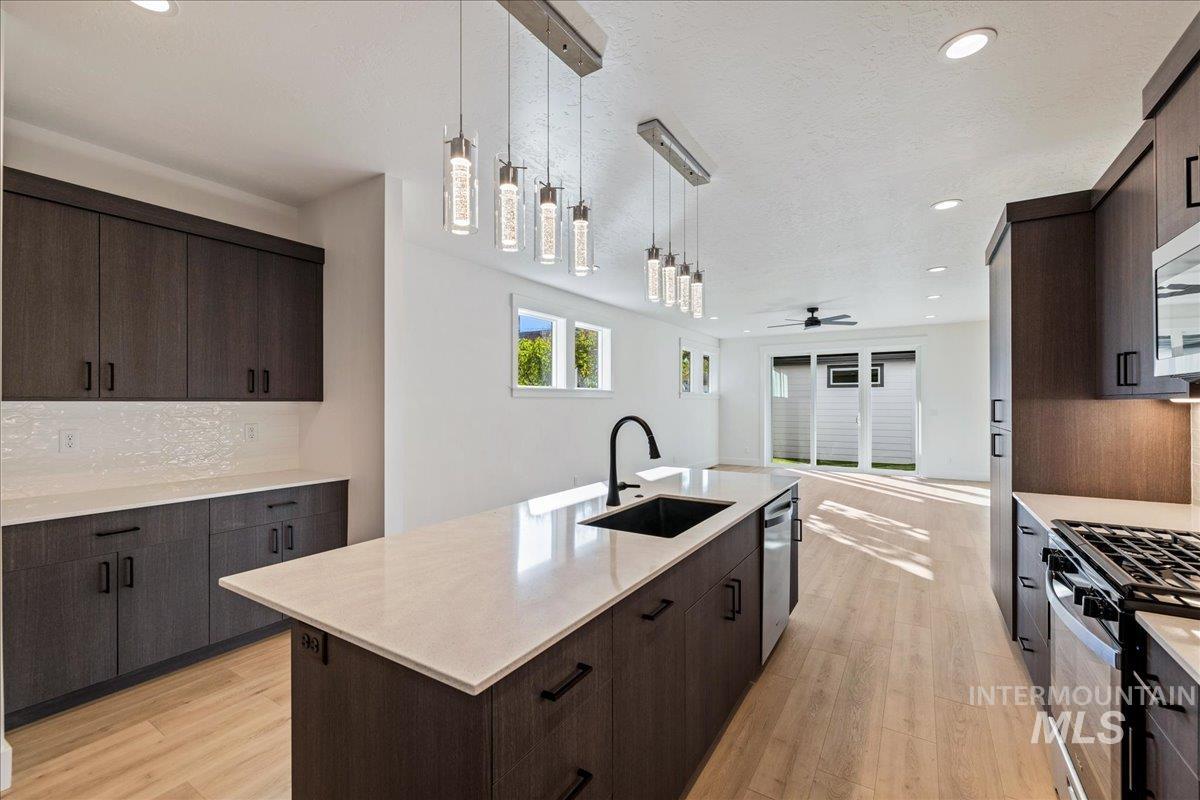 Kitchen with dark brown cabinets, light wood finished floors, pendant lighting, a center island with sink, and recessed lighting