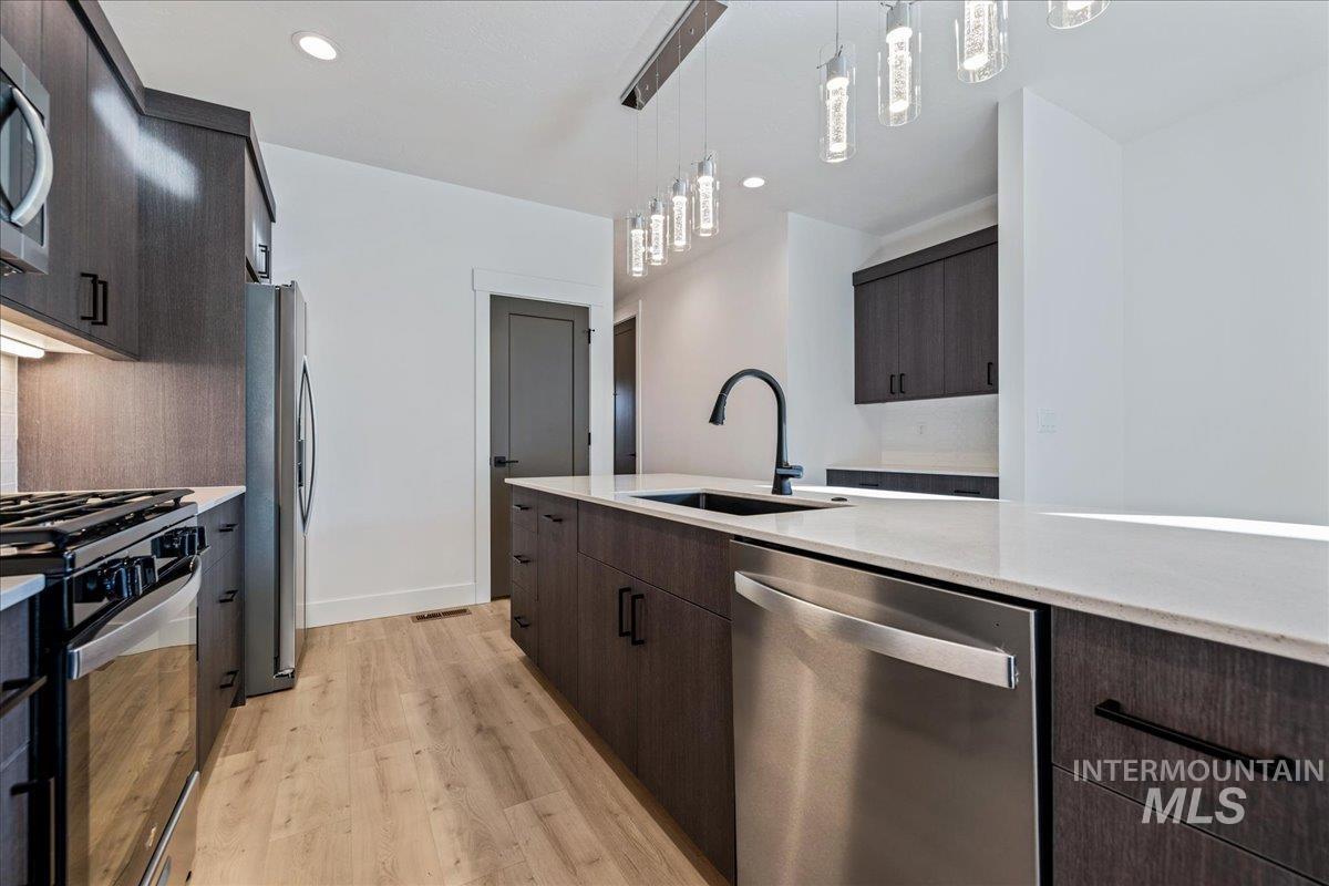 Kitchen with stainless steel appliances, light wood-style flooring, modern cabinets, dark brown cabinetry, and decorative light fixtures