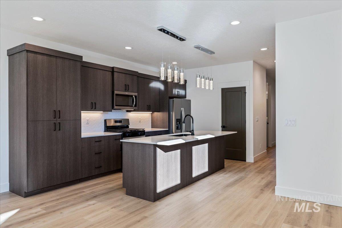 Kitchen with a center island with sink, pendant lighting, stainless steel appliances, dark brown cabinets, and recessed lighting