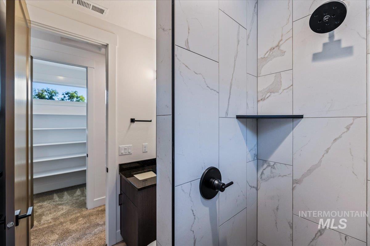 Bathroom featuring tiled shower, vanity, and dark carpet