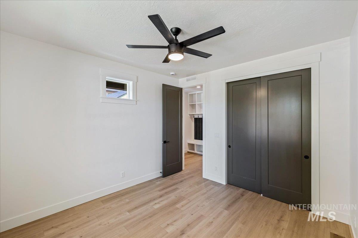 Unfurnished bedroom featuring a textured ceiling, a closet, light wood-style floors, and a ceiling fan