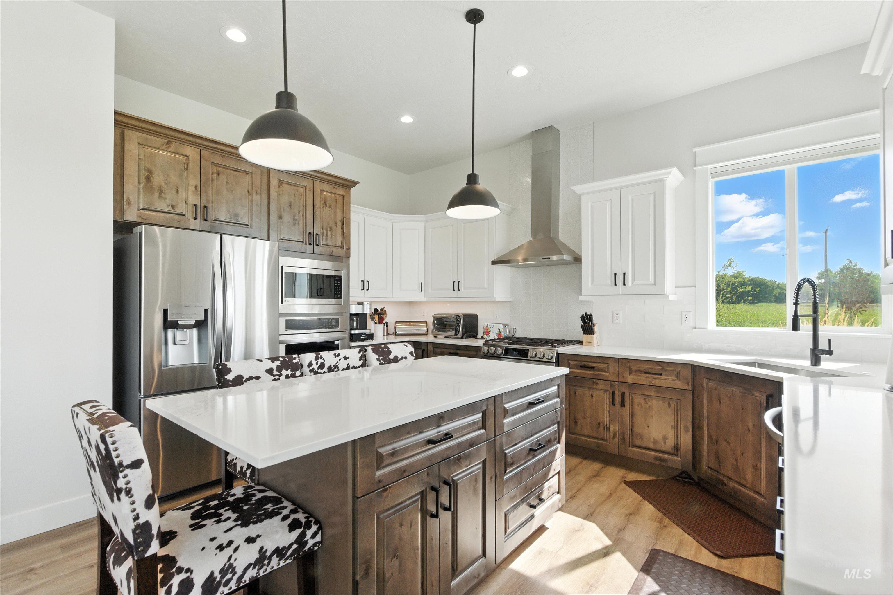 Kitchen with stainless steel appliances, wall chimney exhaust hood, light wood-style flooring, recessed lighting, and light countertops