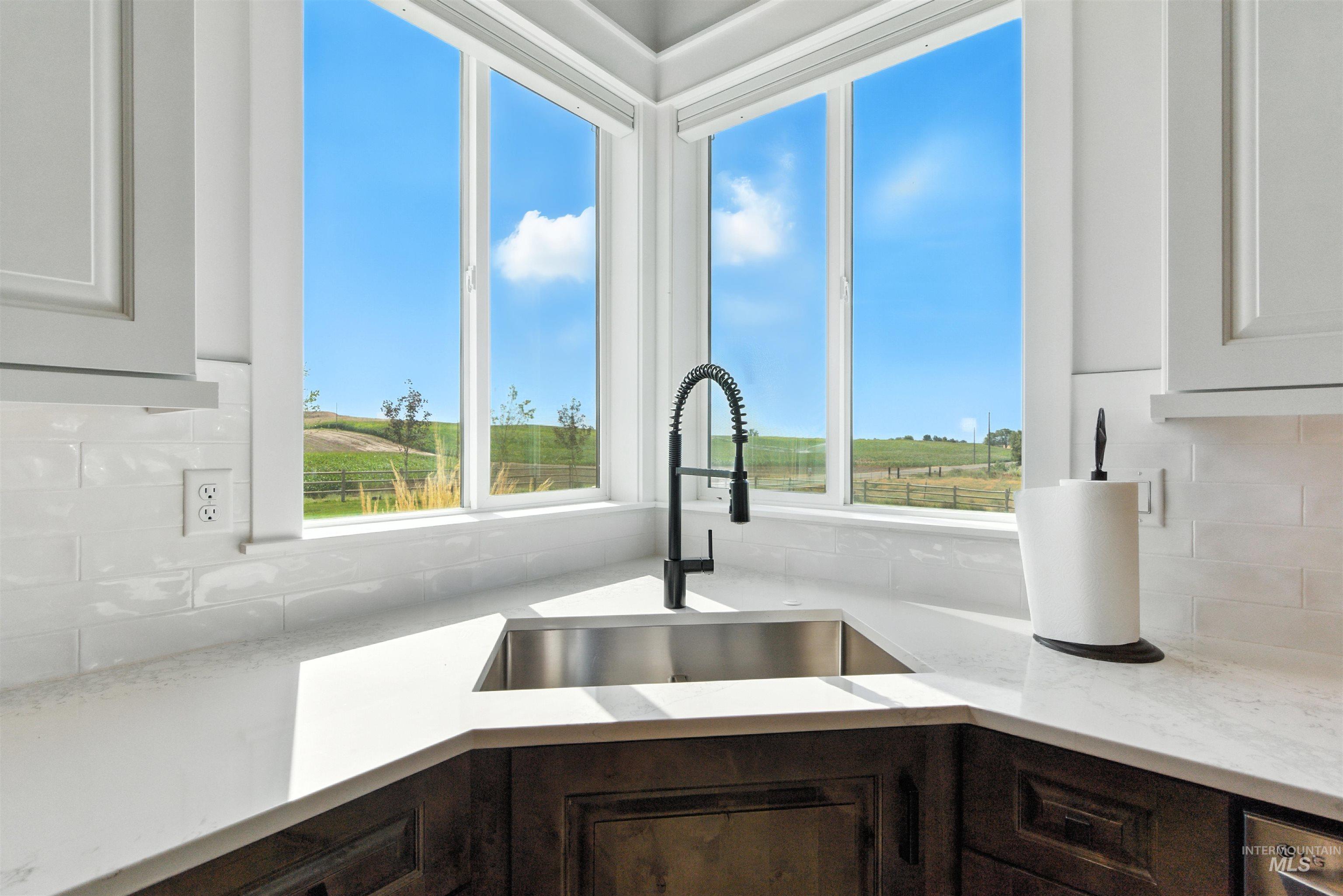 Kitchen view of decorative backsplash, dark brown cabinets, light stone counters, and white cabinets