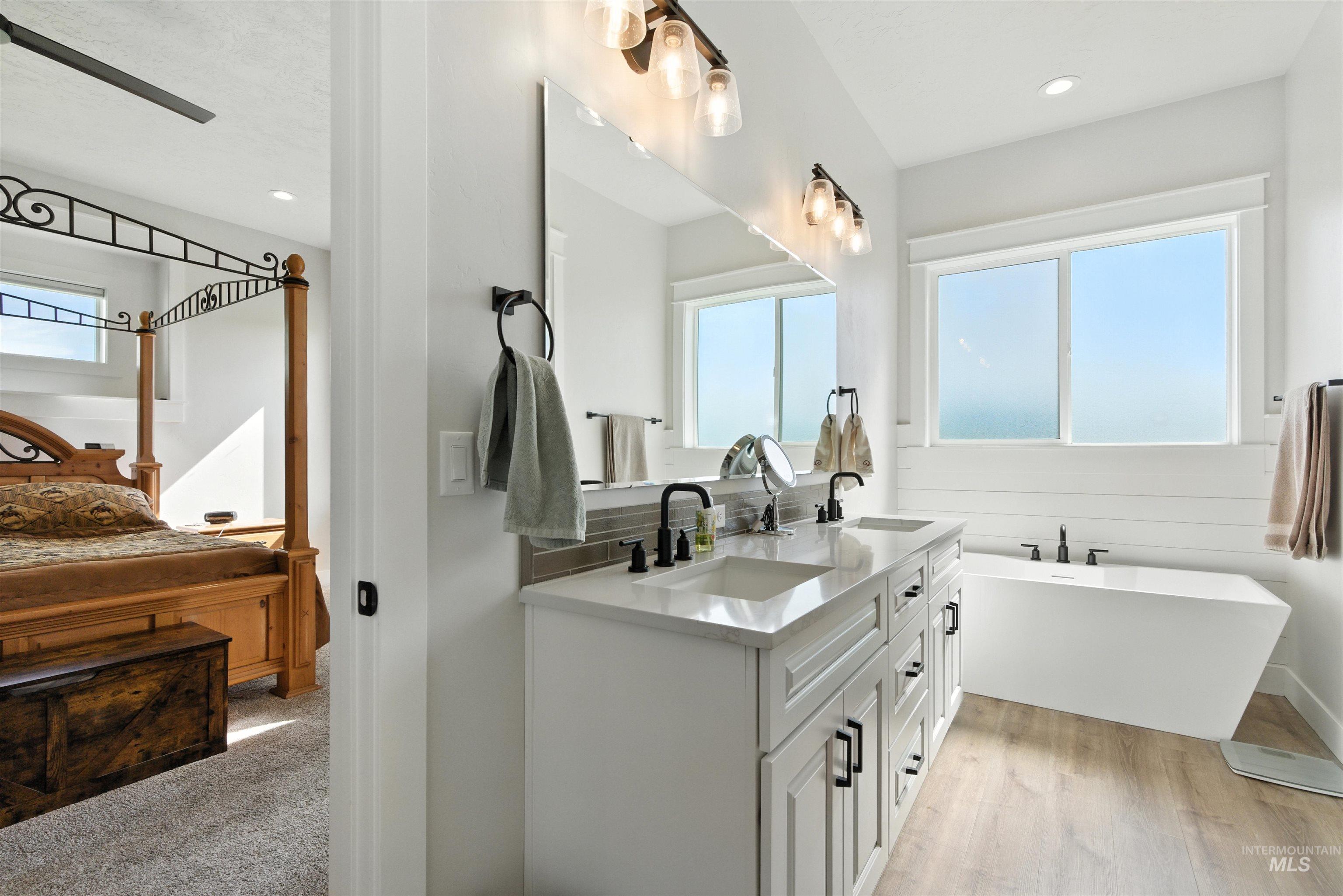 Full bathroom featuring double vanity, a freestanding tub, wood finished floors, and recessed lighting