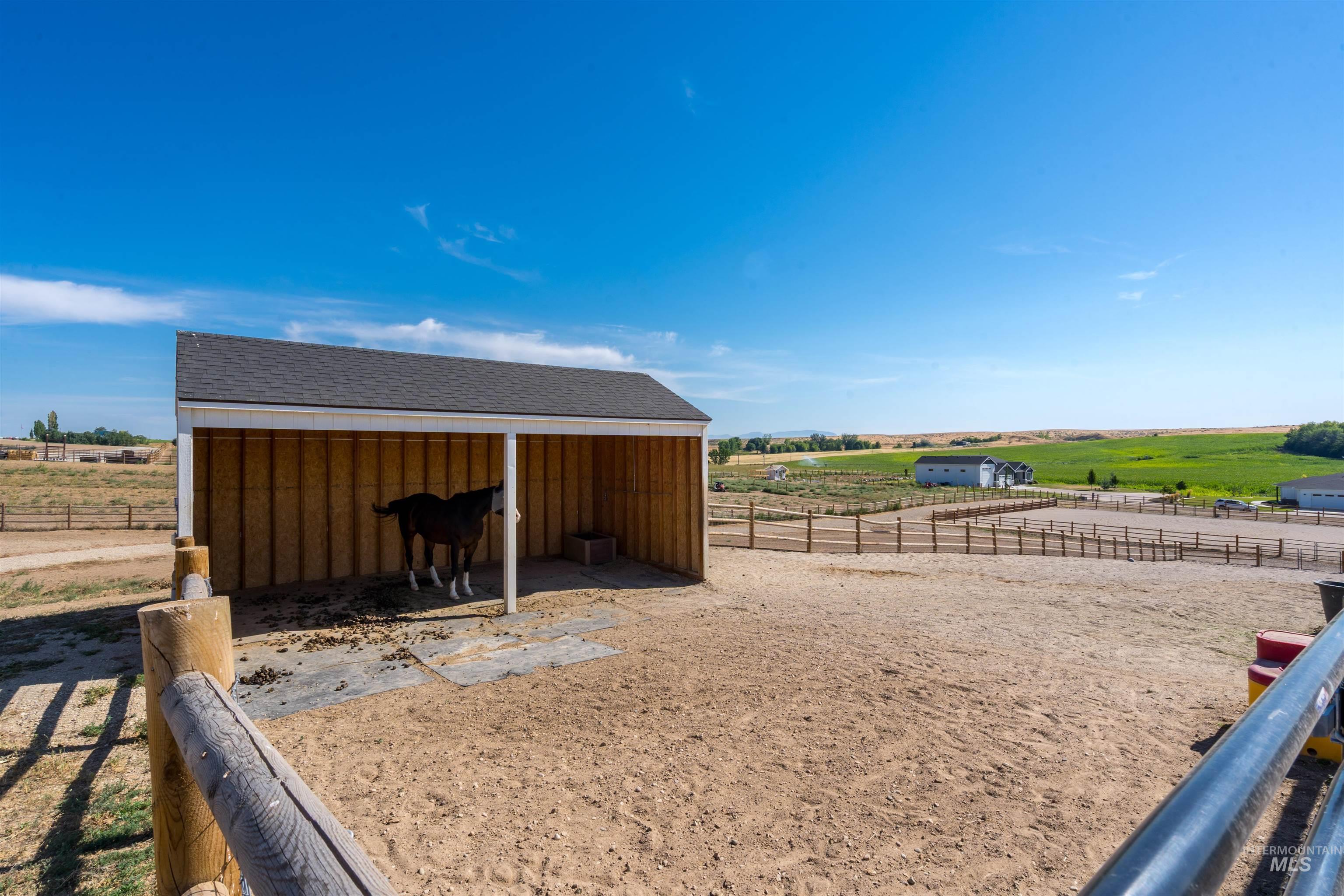 View of yard featuring a view of countryside, an outdoor structure, an exterior structure, and an outdoor riding arena